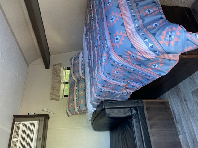 Step into this cozy RV rental bedroom, featuring a vibrant patterned bedspread, window, and air conditioning unit.. Keystone RV Springdale 2019