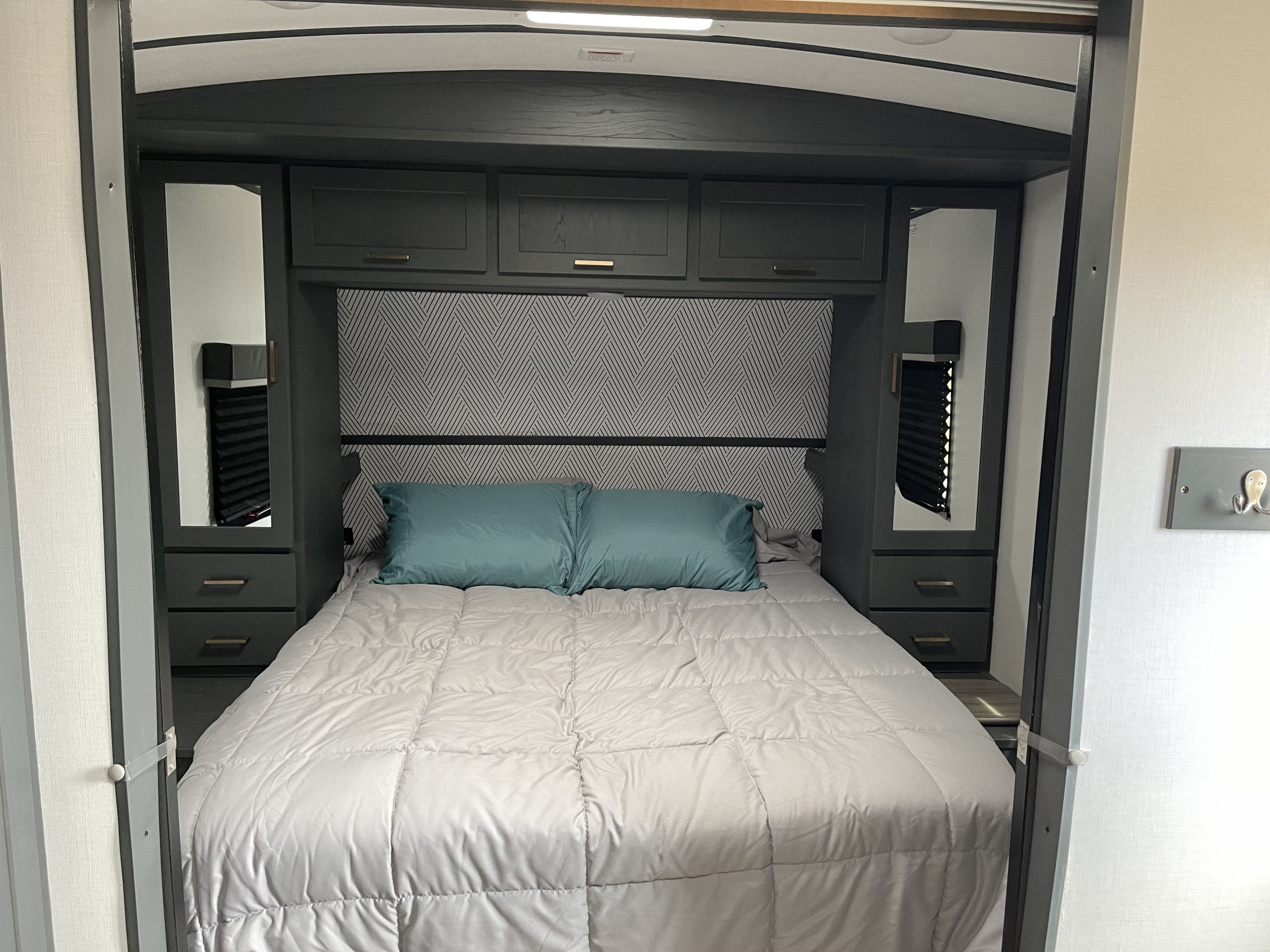 Comfortable RV rental bedroom featuring a bed, dark grey built-in cabinetry, and a patterned headboard.. keystone rv Bullet 2022