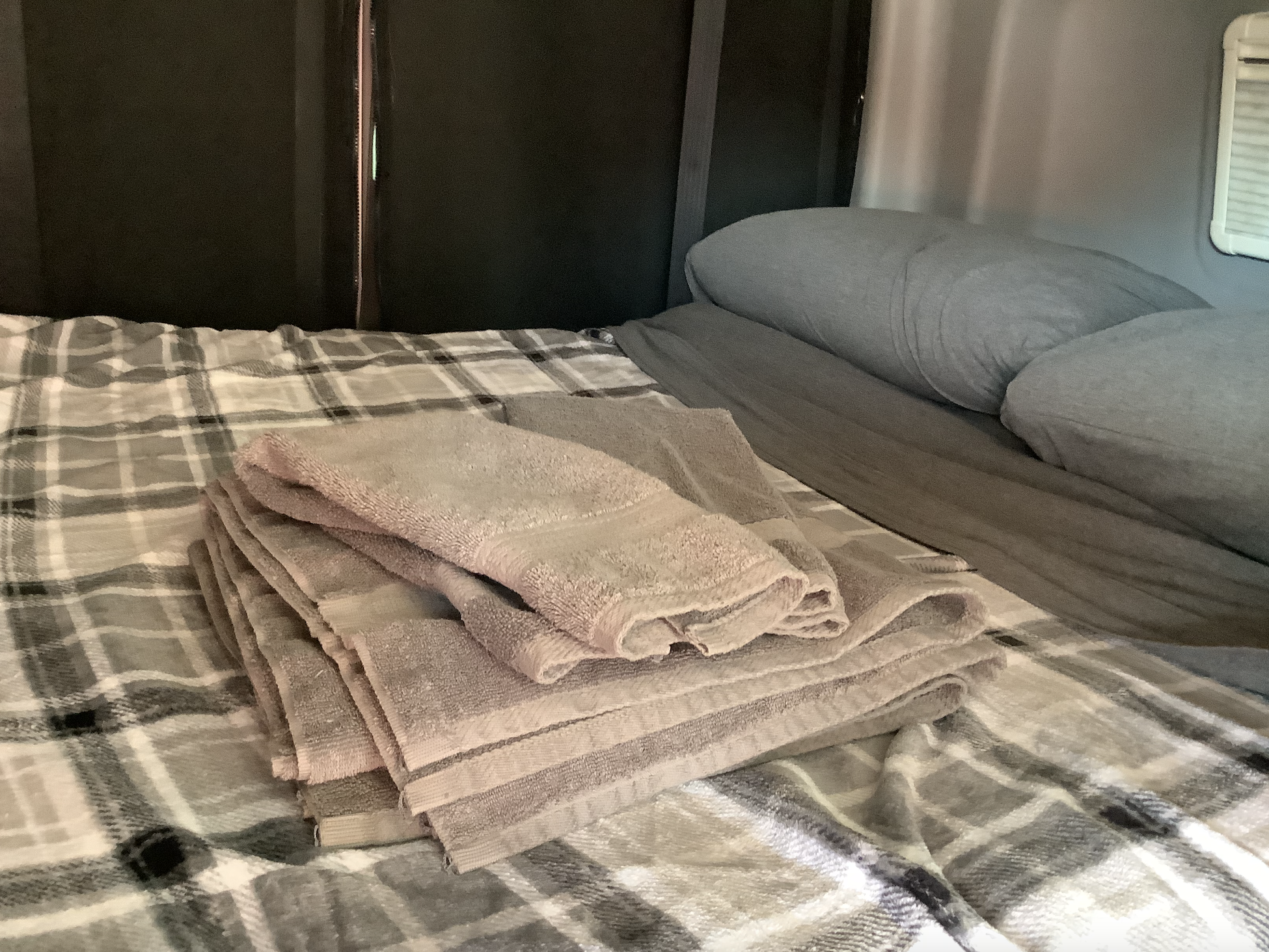 Comfortable RV rental bed with plaid blanket and fresh towels, offering cozy travel accommodations.. Winnebago Revel 2019