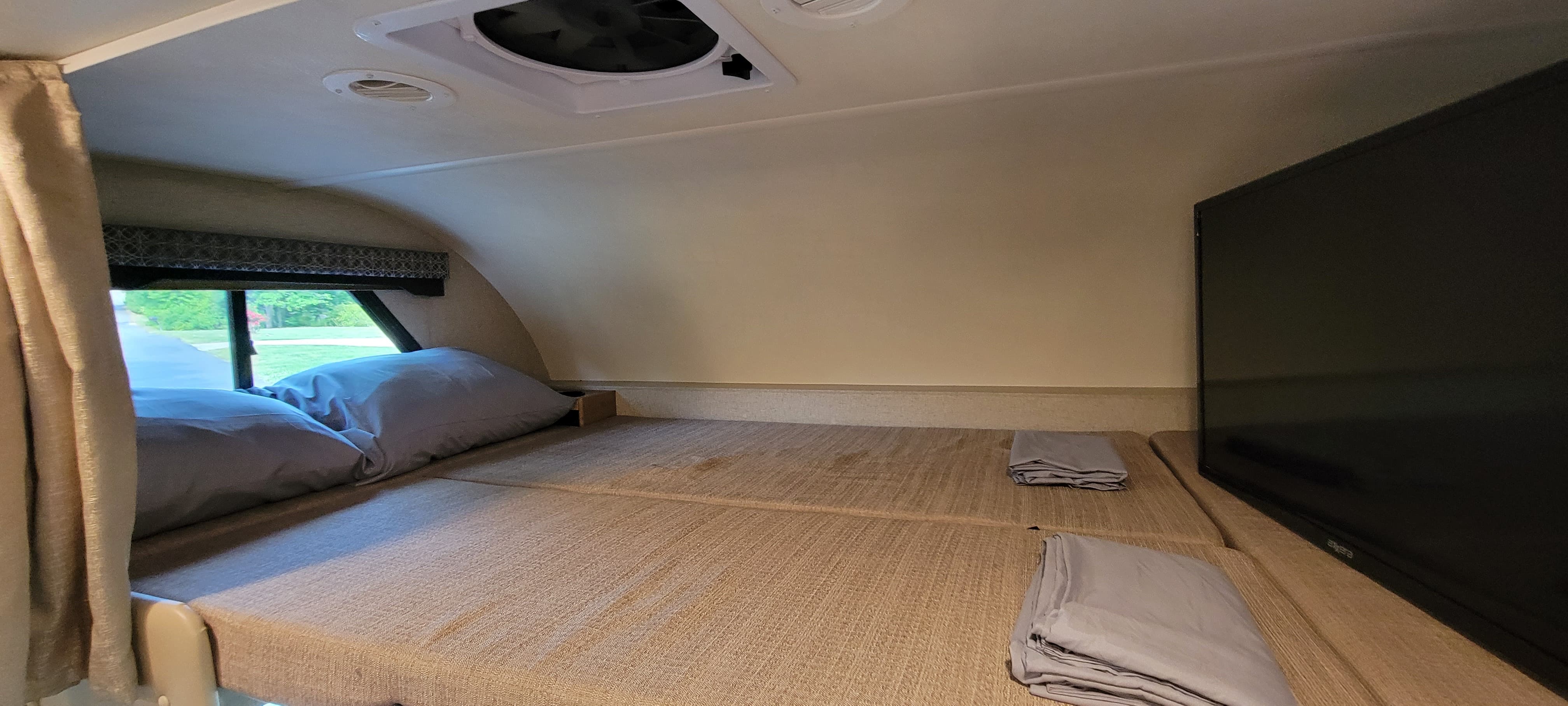RV rental cab-over bunk features comfy bedding, window views, and a TV, ideal for cozy stays.. Thor Four Winds 2020