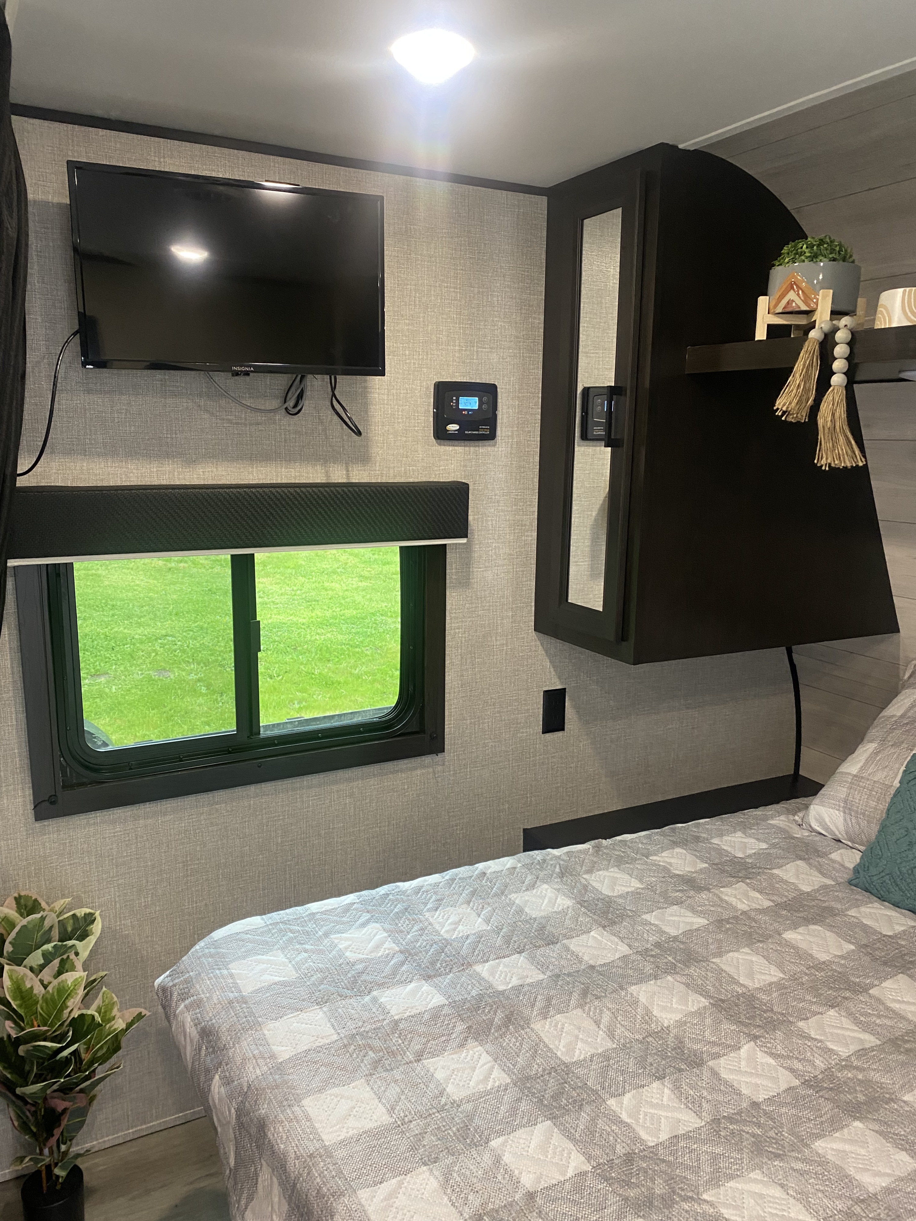 Cozy RV rental interior: bedroom with TV, window to green, solar panel control, and plaid bed. Perfect for trips.. Jayco Jay Flight SLX 8 2022