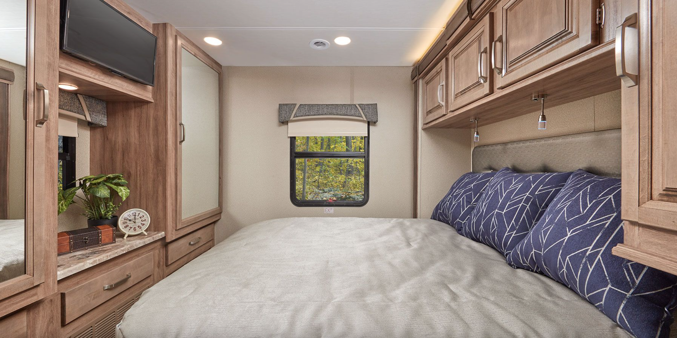 Cozy RV rental bedroom features a comfy bed, window with nature views, and ample storage, ideal for road trips.. Jayco Greyhawk 2020