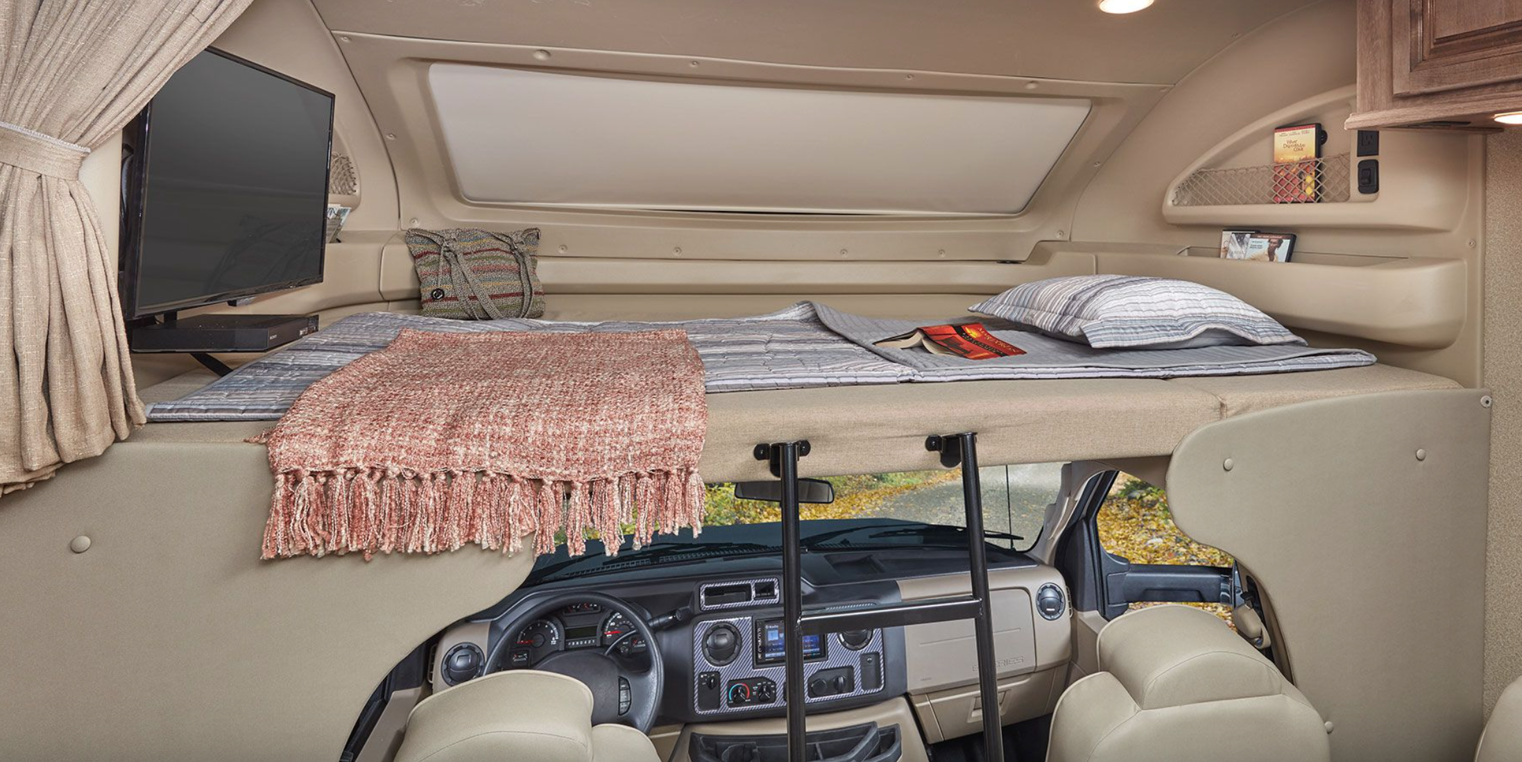 Inside an RV rental: a spacious cab-over bunk with a cozy bed, TV, and ladder overlooking the driver's cockpit.. Jayco Greyhawk 2020