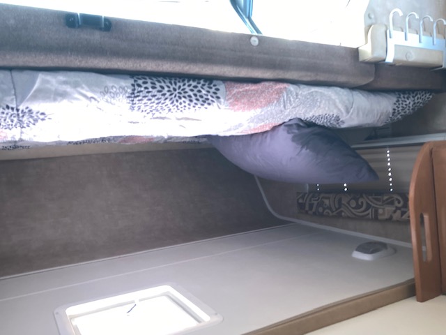 Compact RV rental sleeping area with a bunk bed, patterned comforter, and a purple pillow over a lower bed with a vent.. Coachman Freelander 2013