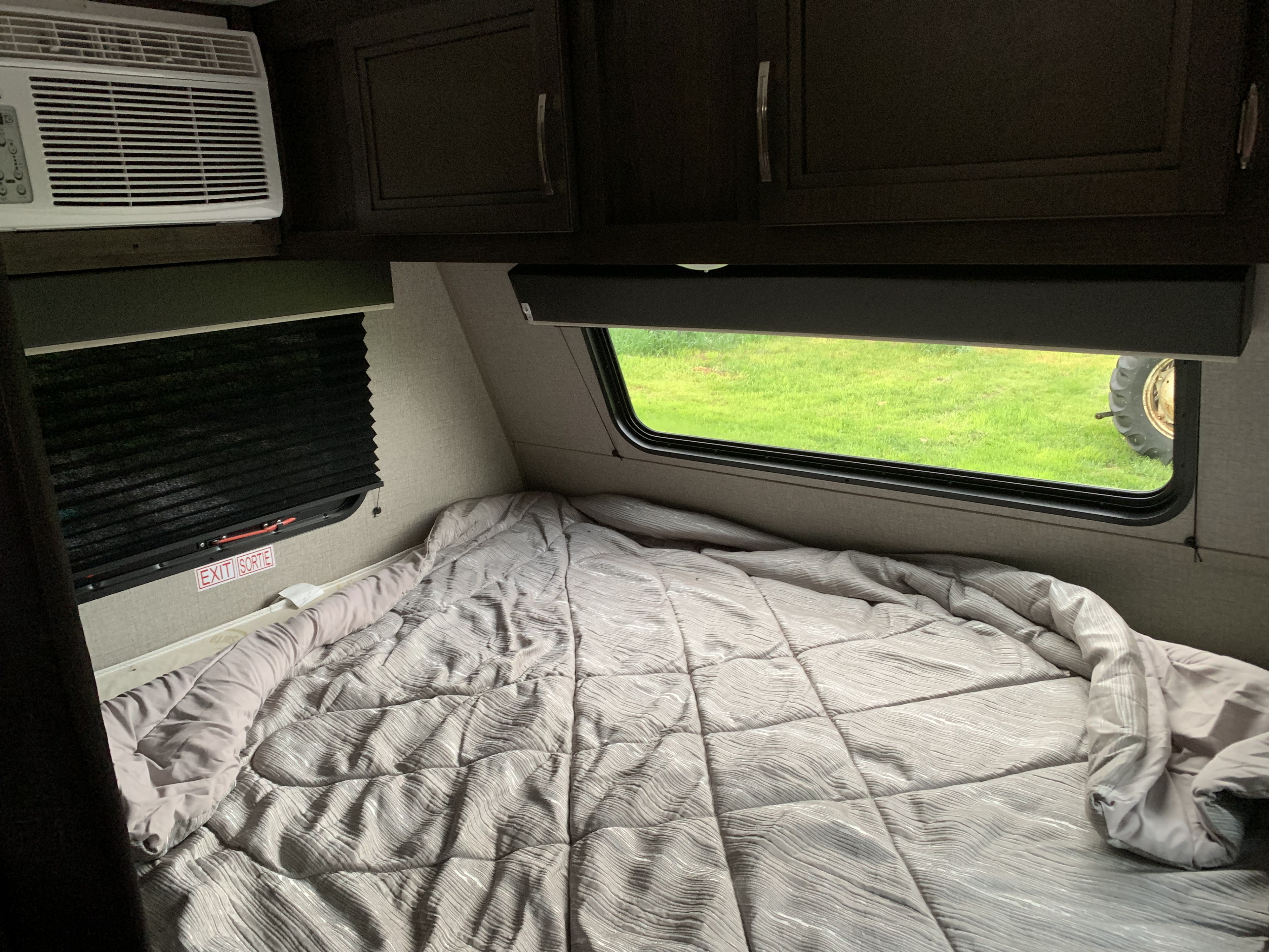 RV rental camper interior: cozy bed, AC unit, cabinets, and window with a view of green grass and a large tire outside.. Jayco Jay Flight 2020