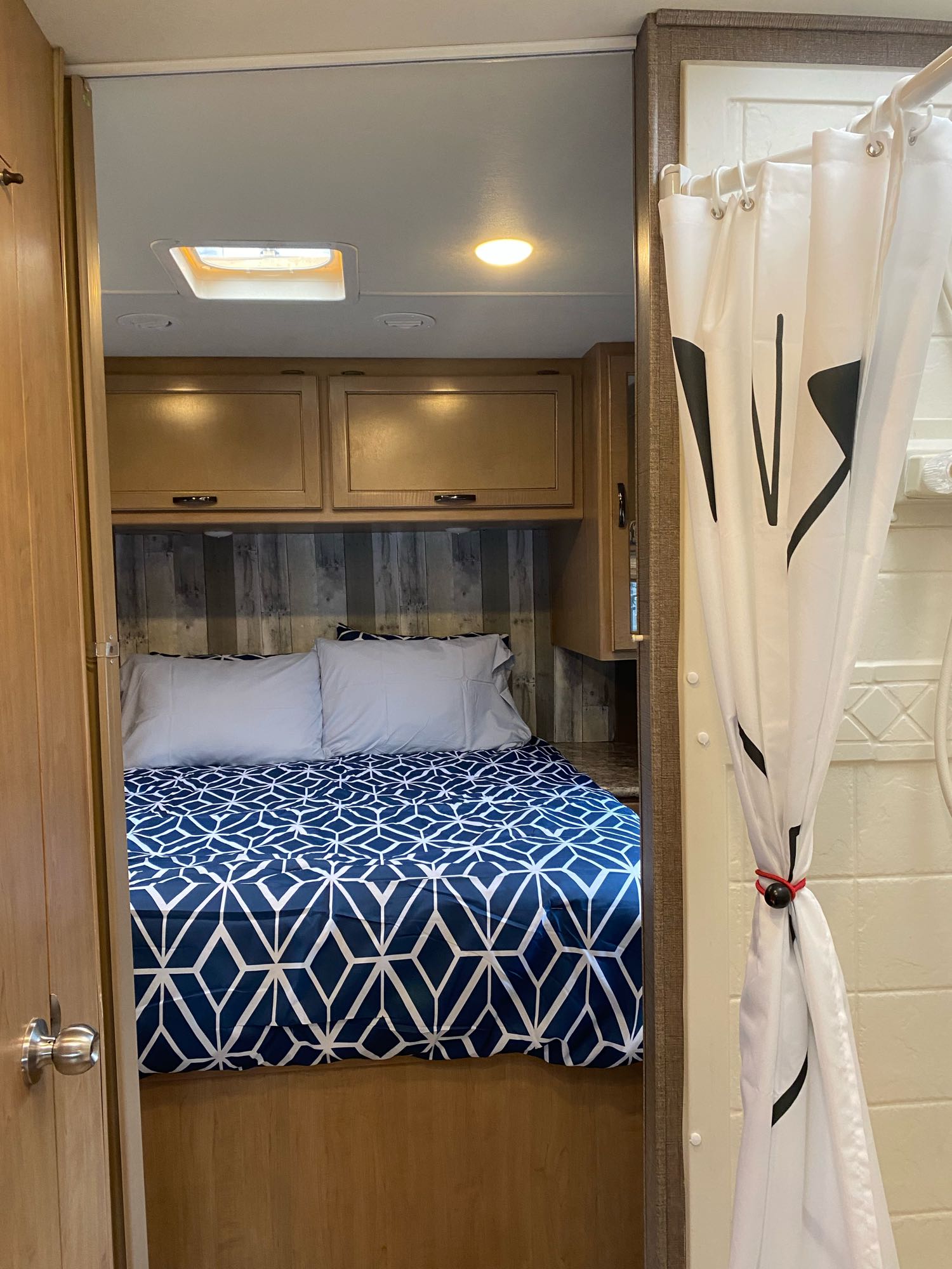Explore this RV rental interior, featuring a cozy bedroom with blue geometric bedding and an adjacent shower area.. Thor Four Winds 2019
