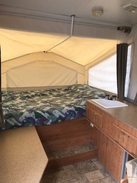 Compact RV rental pop-up camper interior, with a bed, kitchenette sink, and seating area for your travels.. Forest River Rockwood Freedom 2007