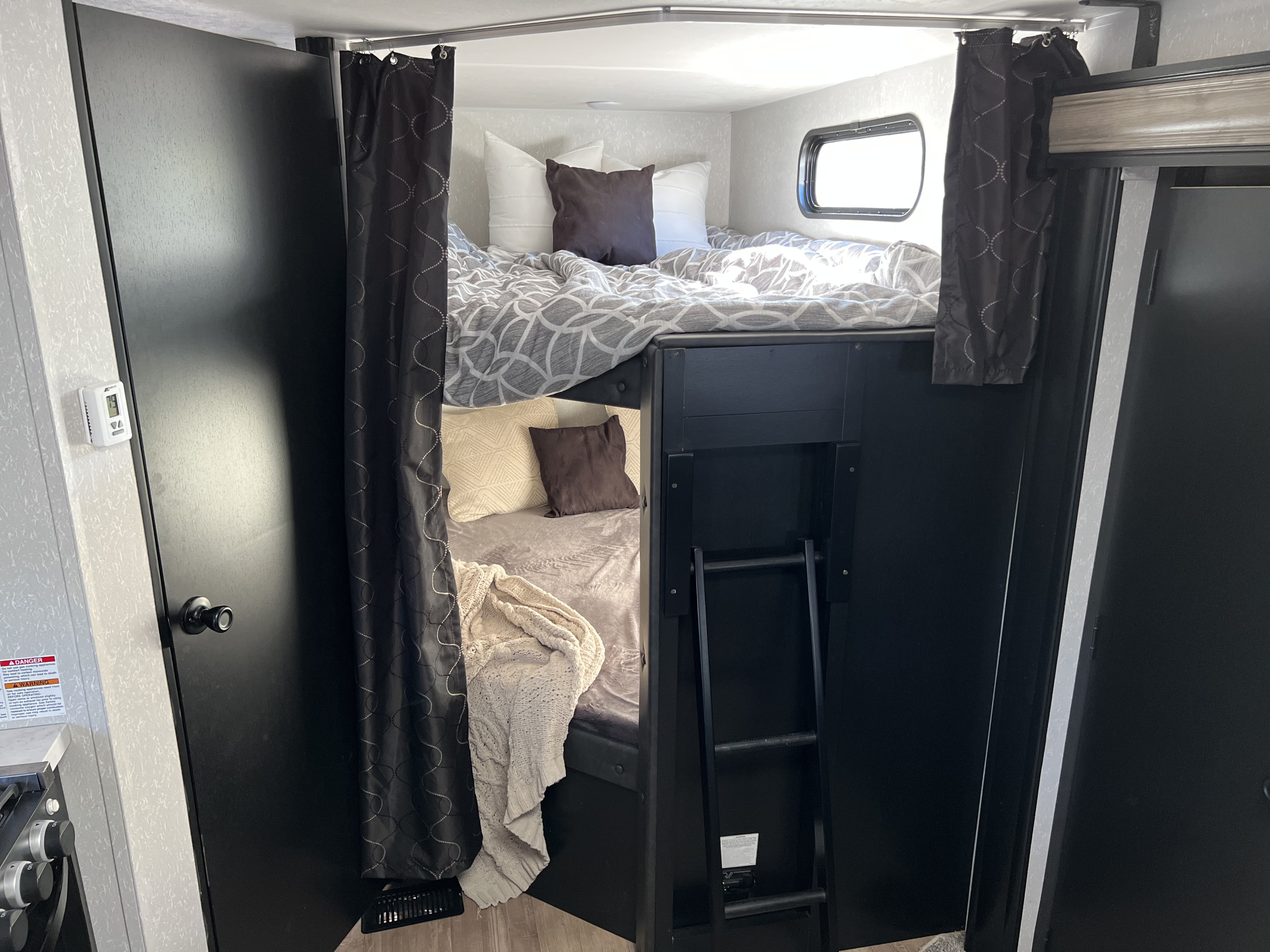 Inside an RV rental, discover comfortable bunk beds with patterned bedding, privacy curtains, and a ladder. Black and white decor.. Forest River Cherokee Grey Wolf 2021