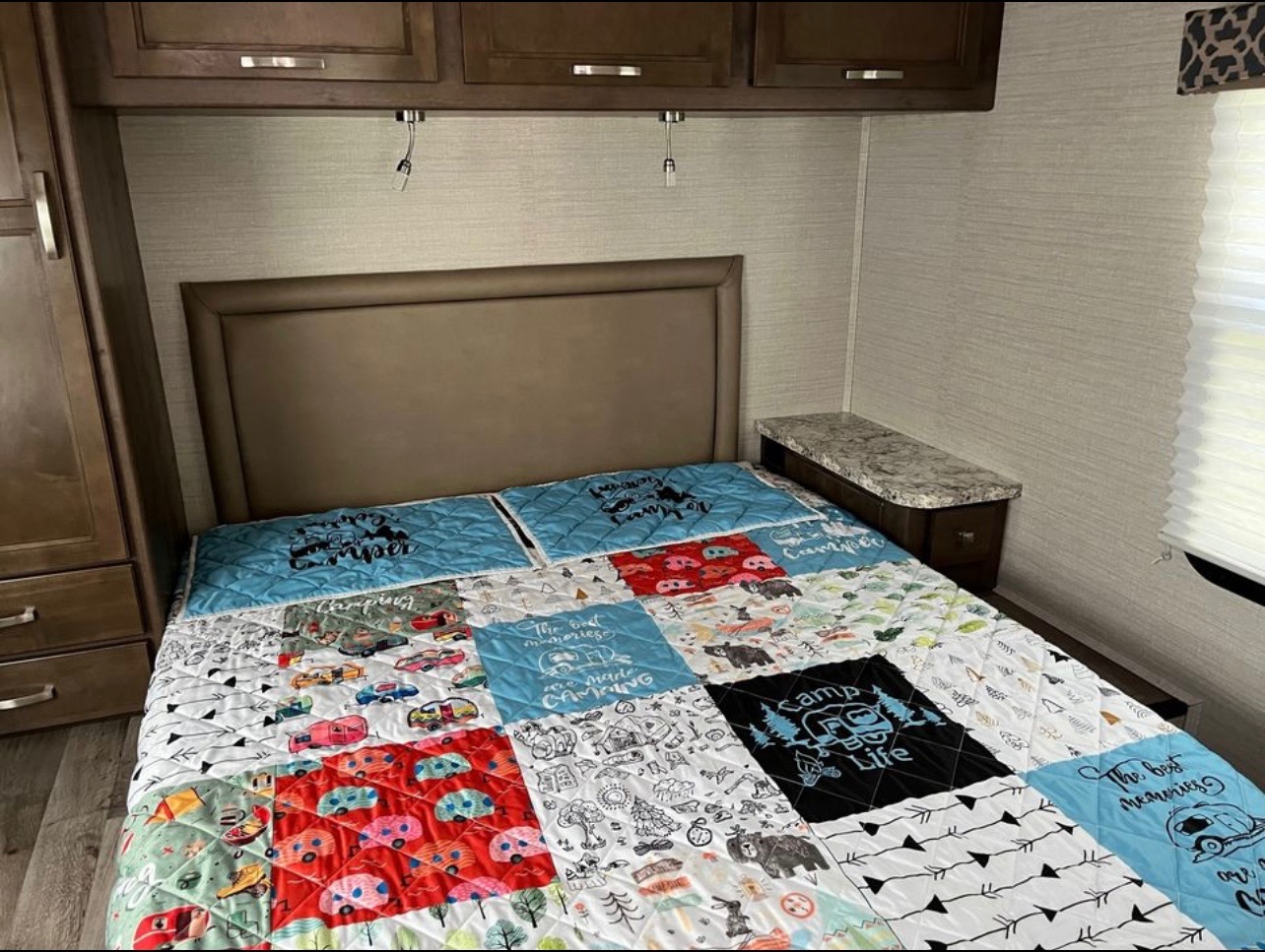 Relax in this RV rental bedroom featuring a colorful camping quilt and practical overhead storage and nightstand.. Jayco Redhawk 2021