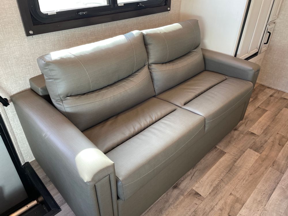 Comfortable light gray sofa in a modern RV rental interior. Ideal for relaxing and travel comfort.. Entegra Coach Odyssey 31F 2022