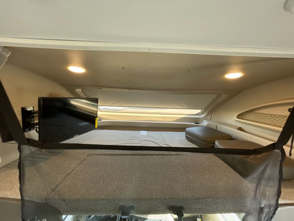 RV rental cab-over bunk featuring a comfortable bed, mounted TV, and overhead lighting for a cozy interior.. Entegra Coach Odyssey 31F 2022