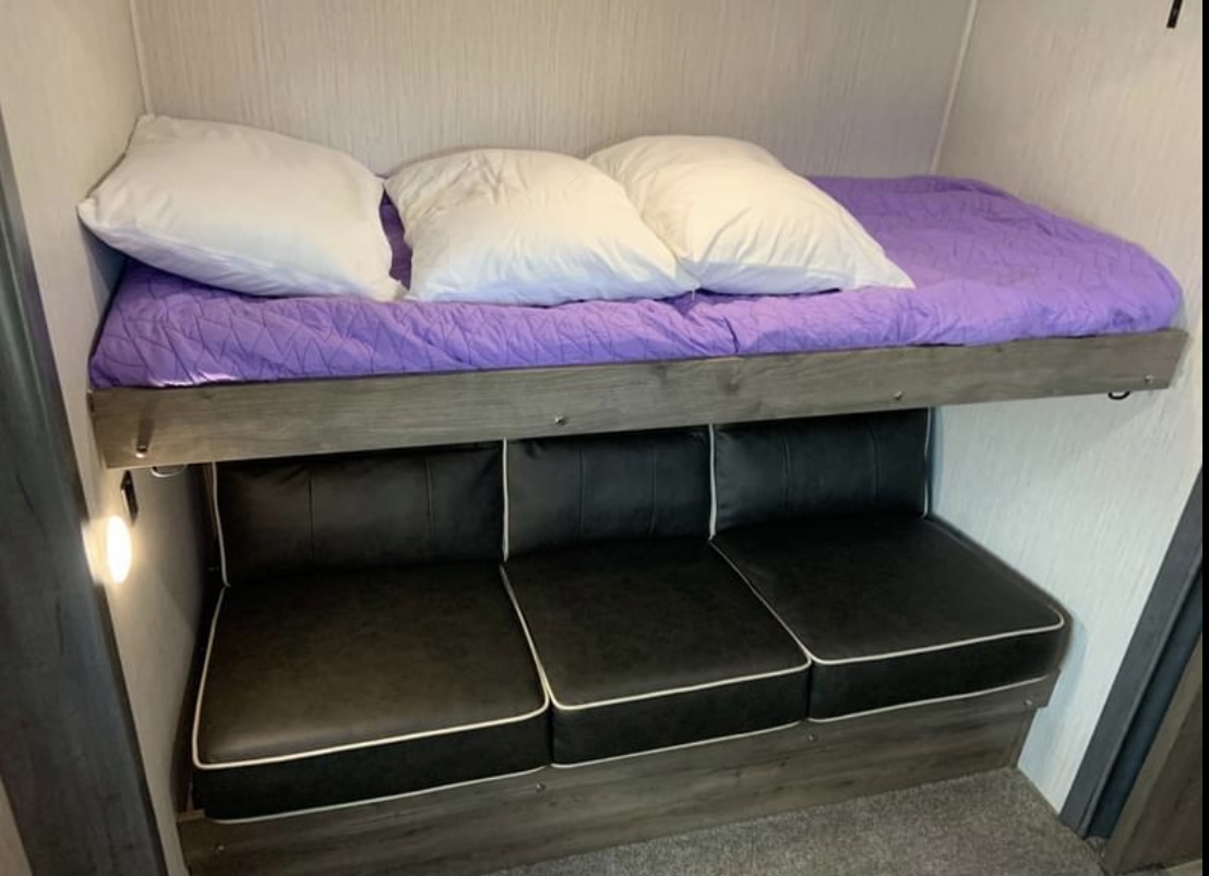 Compact RV rental: Bunk bed with purple comforter, black sofa below.. Forest River Palomino Puma 2020