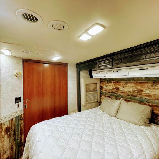 RV rental interior: A cozy bedroom with a quilted bed, rustic wood headboard, and sliding closet.. Fleetwood Expedition 38F 2008