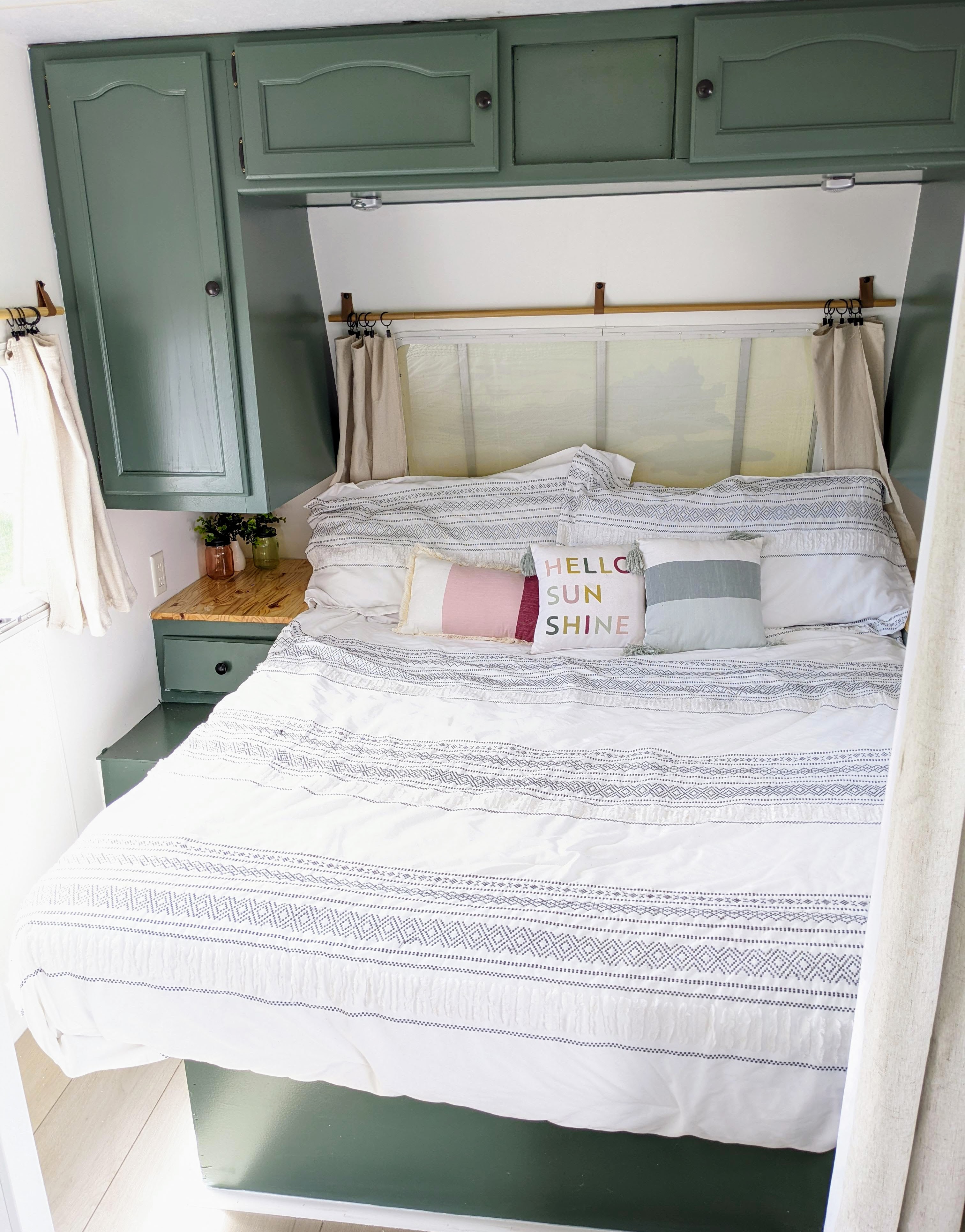 Discover a comfortable RV rental interior: a bedroom with patterned bedding, bright pillows, and sage green cabinets.. Keystone RV Springdale 2003