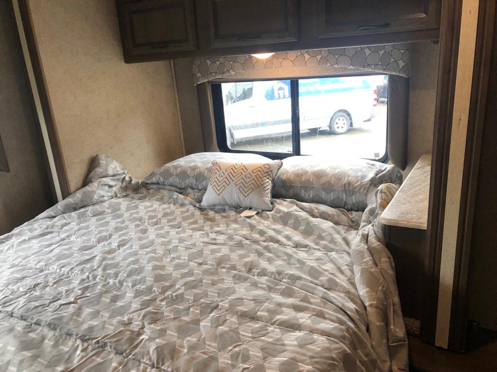 Cozy RV bedroom interior: patterned bed, overhead cabinets, and window view, ideal for your rv rental stay.. Forest River Coachmen Freelander 2018