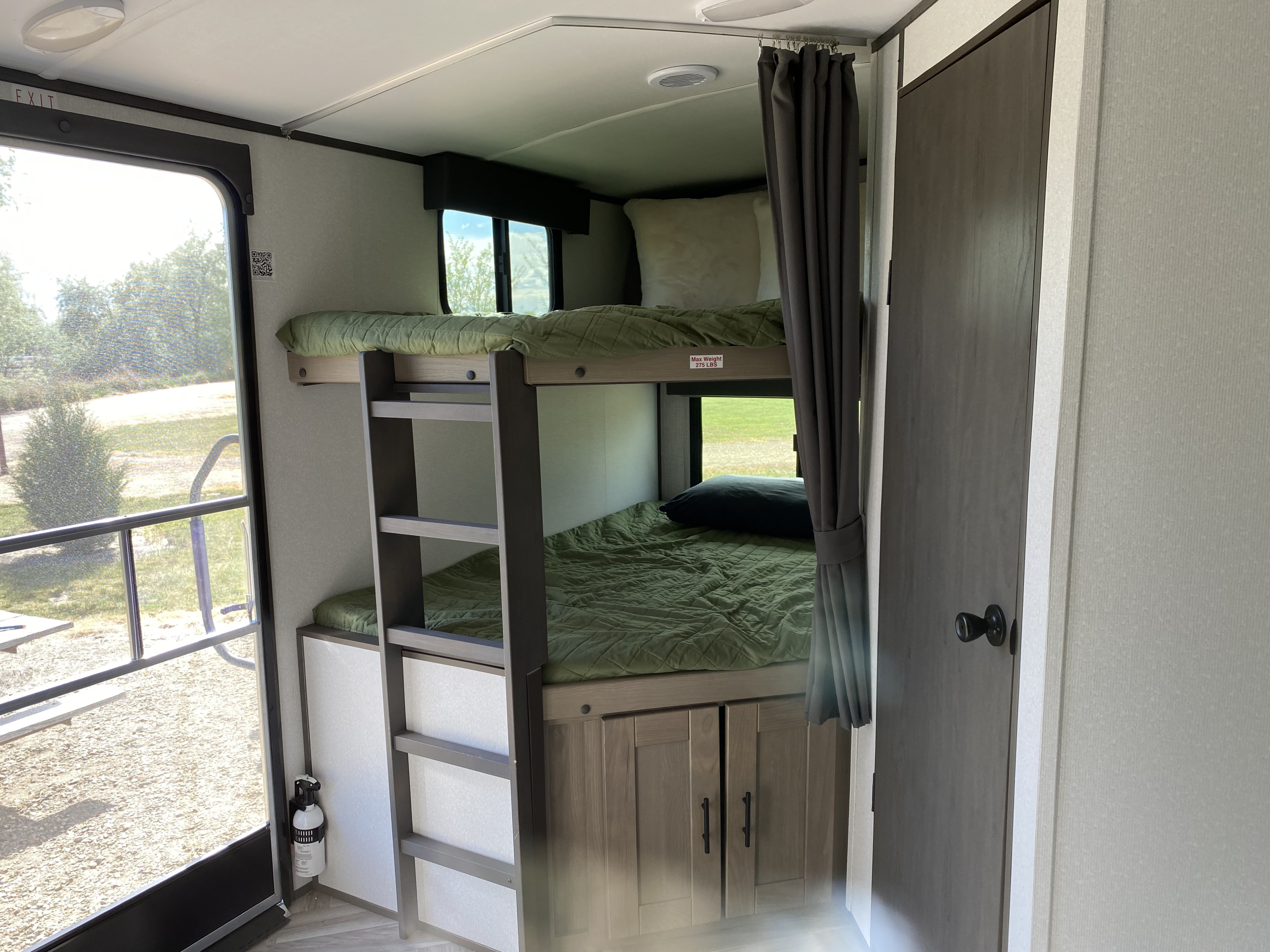 RV rental bunk beds with green bedding, outdoor window view, and fire extinguisher inside for safety.. Cruiser RV M-277BHS 2021
