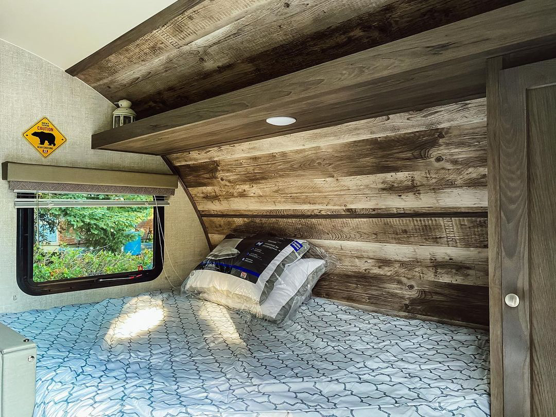 Cozy RV rental bedroom with rustic wood accents, a comfortable bed, and a window view of lush greenery.. Gulf Stream Other 2021