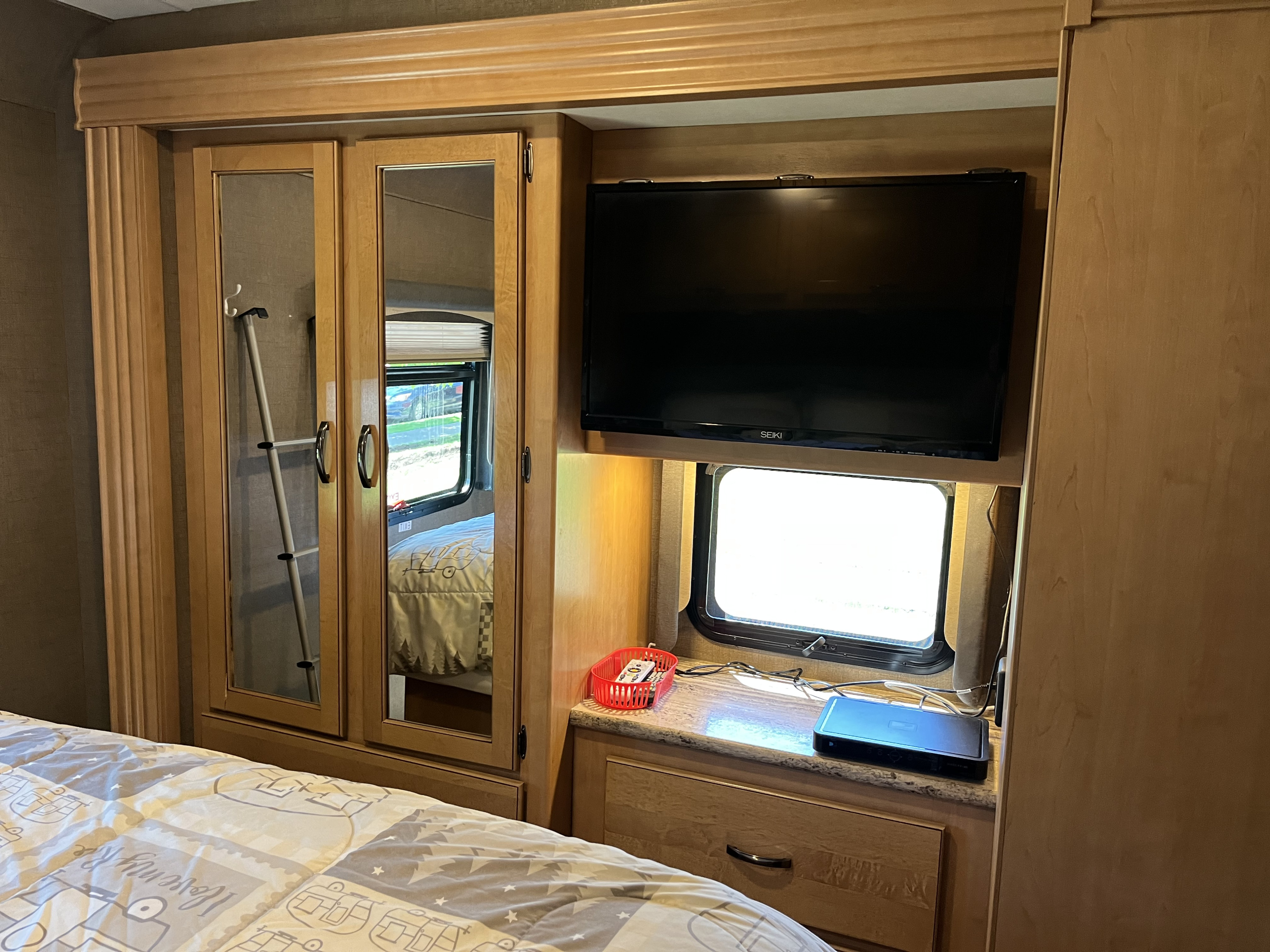 This RV rental bedroom features a comfy bed, wall-mounted TV, window, and mirrored closet.. Thor A.C.E. 2017