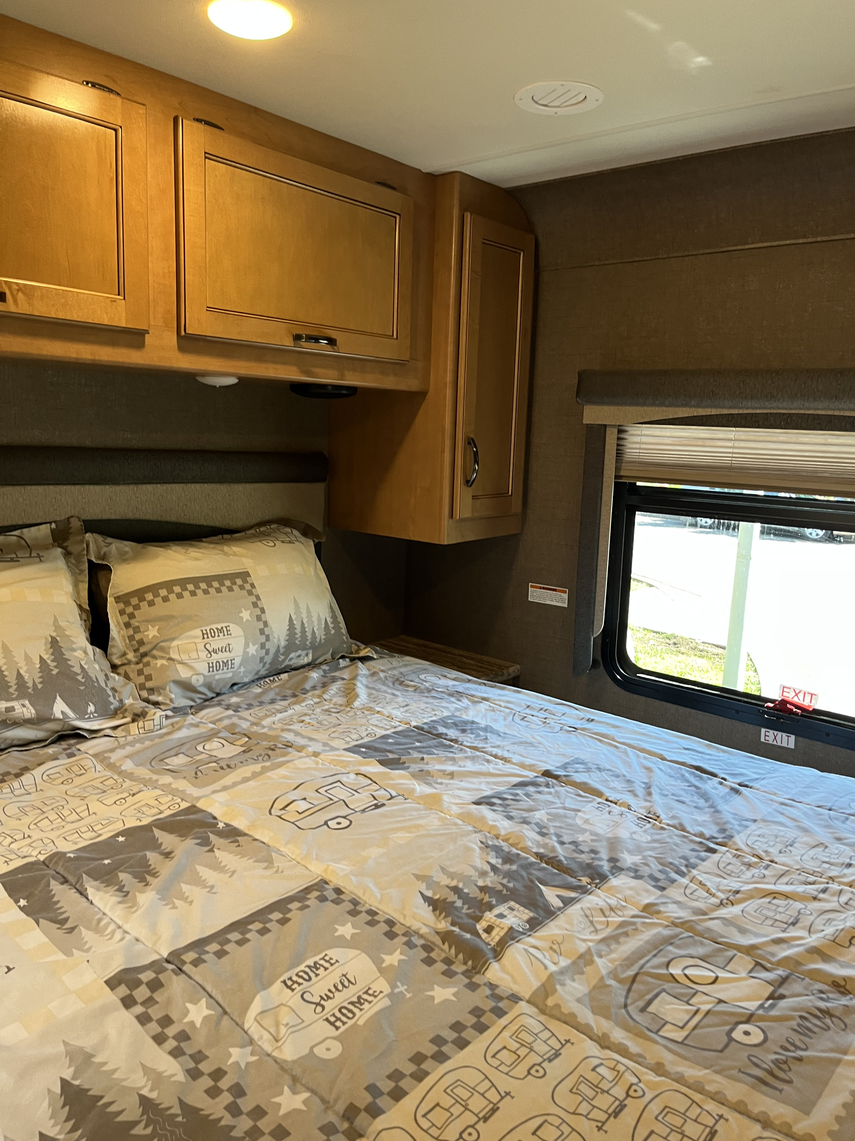 Cozy RV rental bedroom with themed bedding, overhead storage, and window showing an exit.. Thor A.C.E. 2017