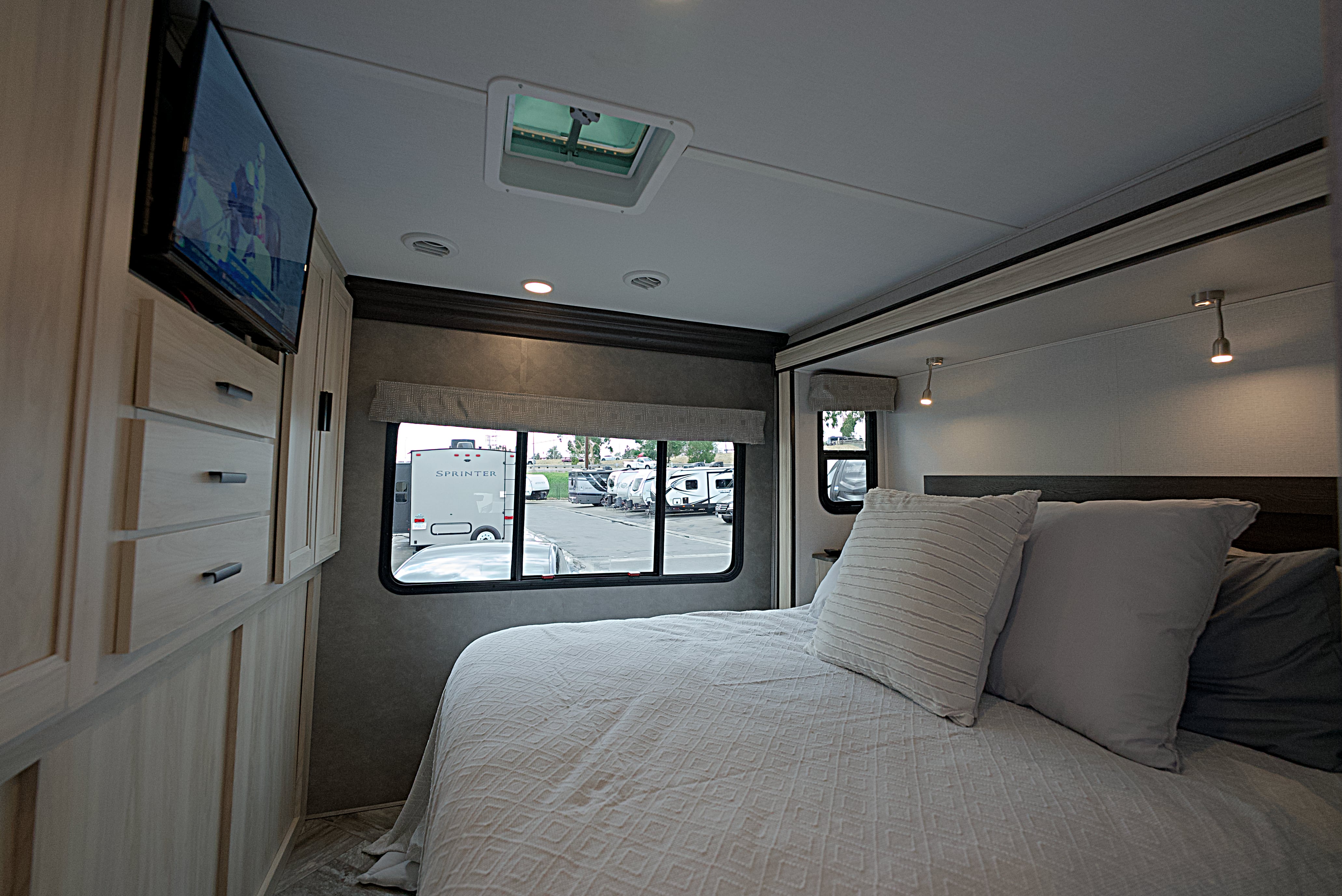 Spacious RV rental bedroom featuring a comfy bed, TV, and window view of an RV lot.. Forest River Sunseeker 2022
