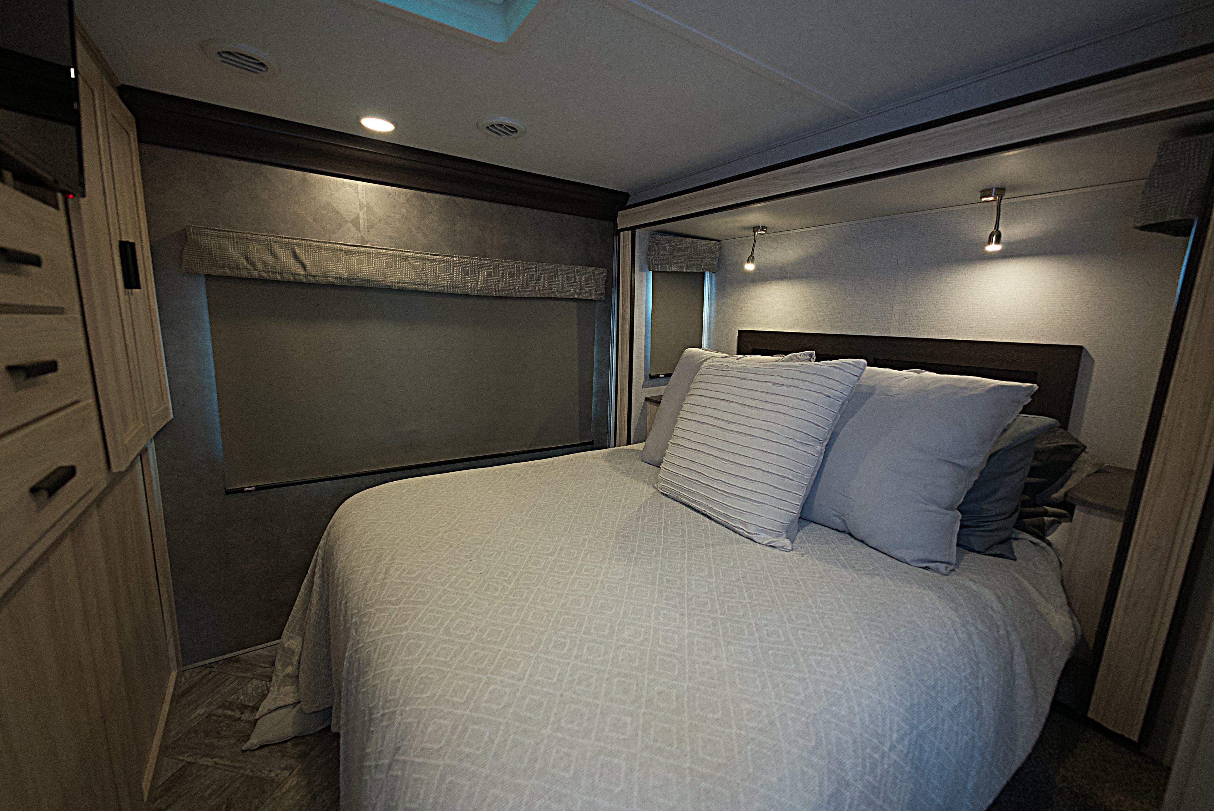 Comfortable RV rental bedroom with a neatly made bed, reading lights, and compact storage for a cozy travel stay.. Forest River Sunseeker 2022