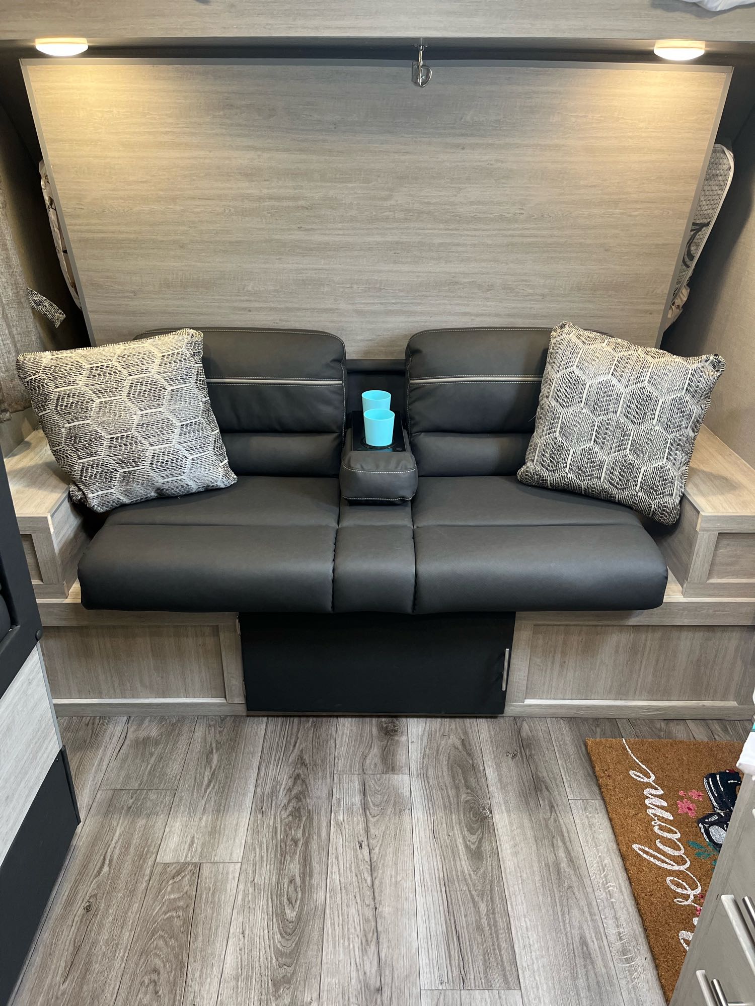 Comfortable RV rental seating area with black sofa, patterned pillows, console, and wood-look floor.. Coachmen Catalina Summit Series 7 2022
