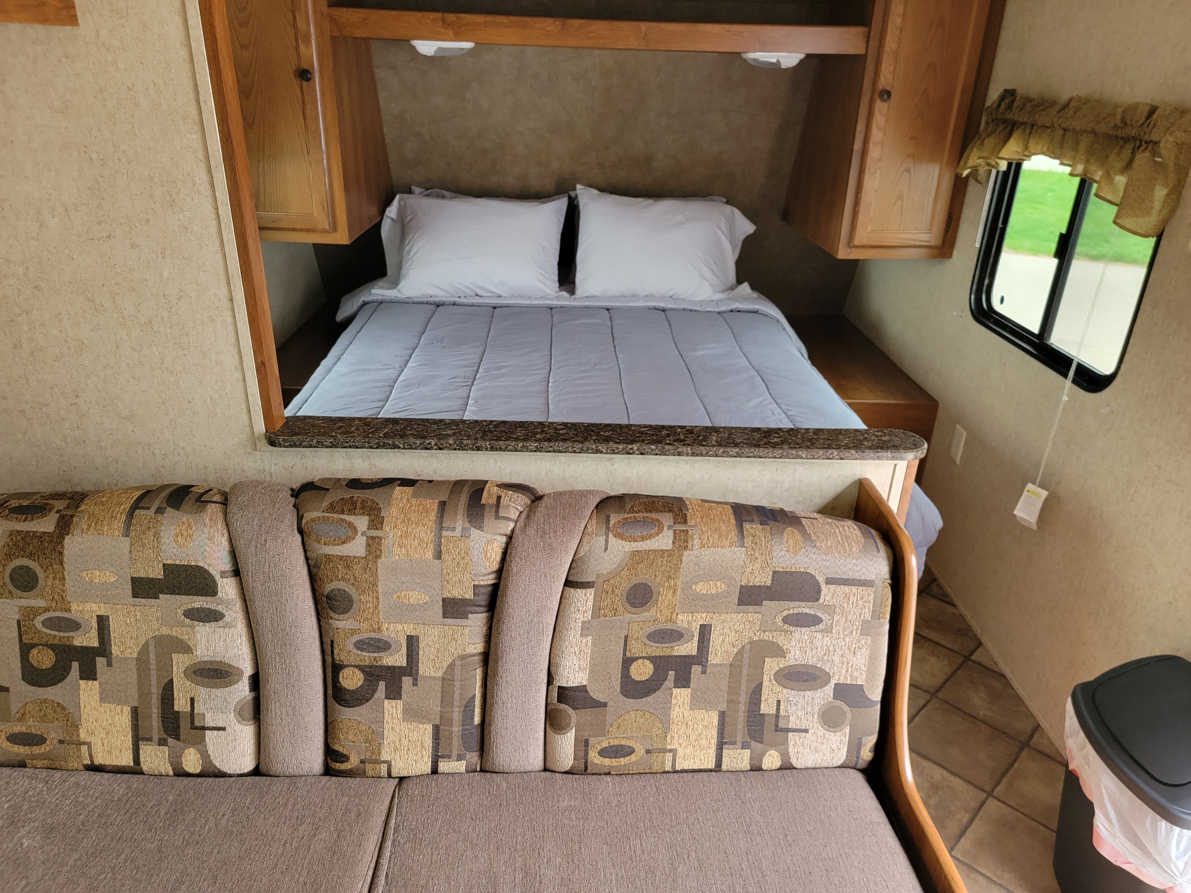 Inside an RV rental: a comfortable bed with light blue bedding, overhead cabinets, and a patterned couch.. Heartland RVs Trail Runner 2013