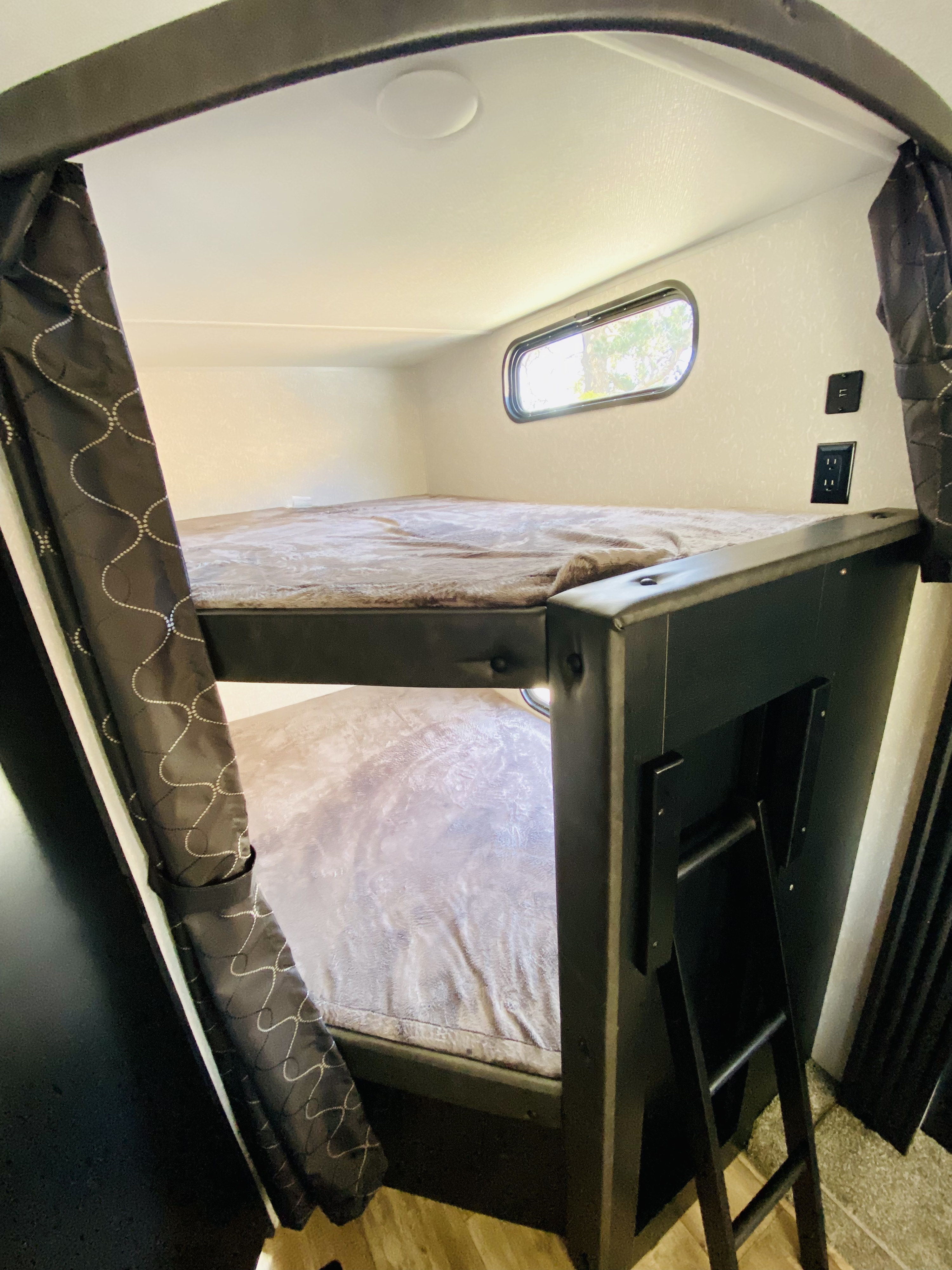 An RV rental's cozy bunk beds, complete with a window, charging outlets, and a ladder for access.. Forest River Cherokee 2022