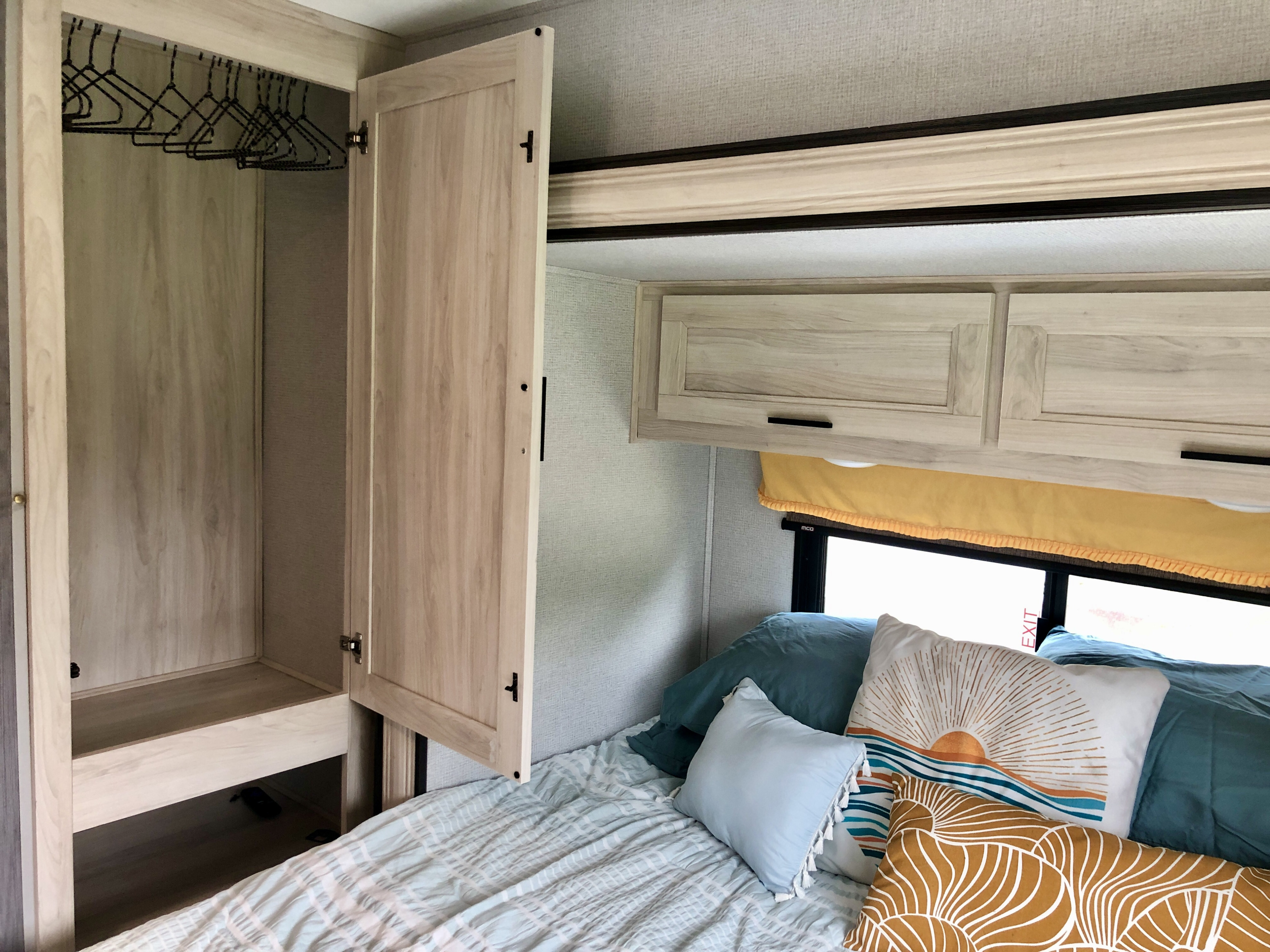 RV rental bedroom interior featuring an open closet with hangers, a cozy bed with decorative pillows, and overhead cabinets.. Forester LE 2020
