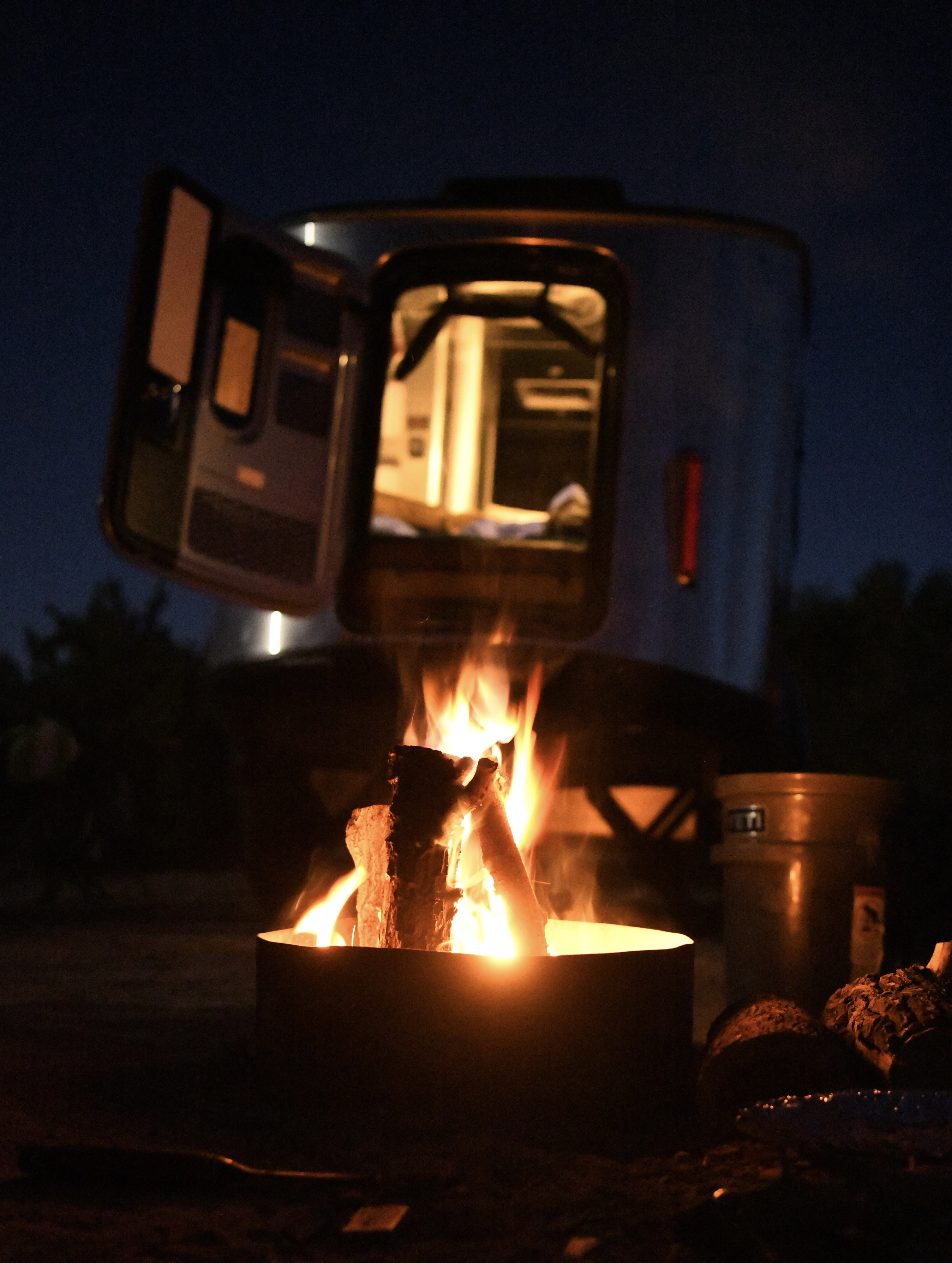 Nighttime RV rental: Warm campfire in front of an illuminated Airstream RV with its door open, inviting a cozy escape.. Airstream Basecamp 2021