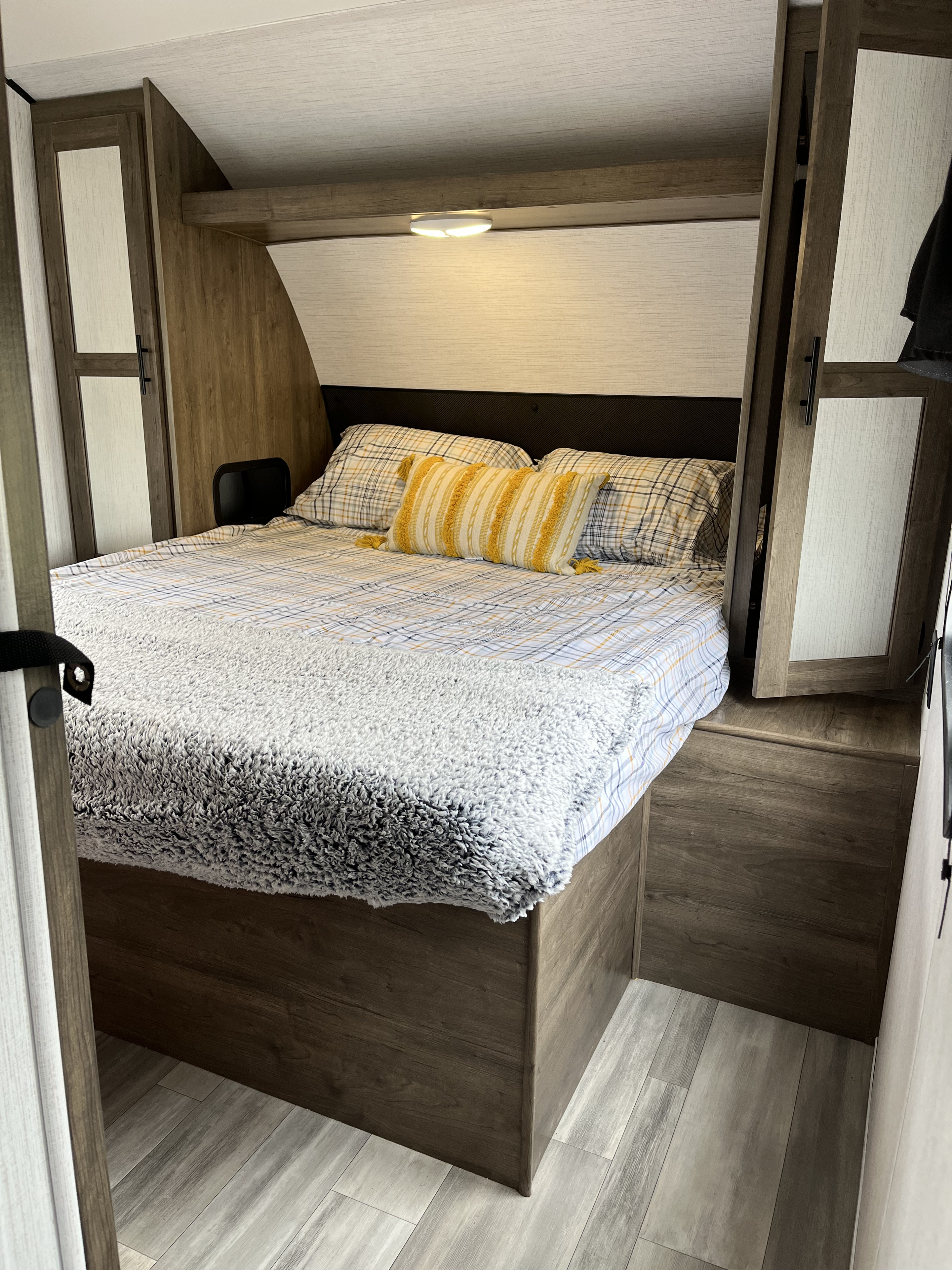 Cozy RV rental bedroom with plaid sheets, a fuzzy blanket, built-in wood cabinetry, and an overhead light.. Heartland Pioneer BH270 Bunkhouse 2022
