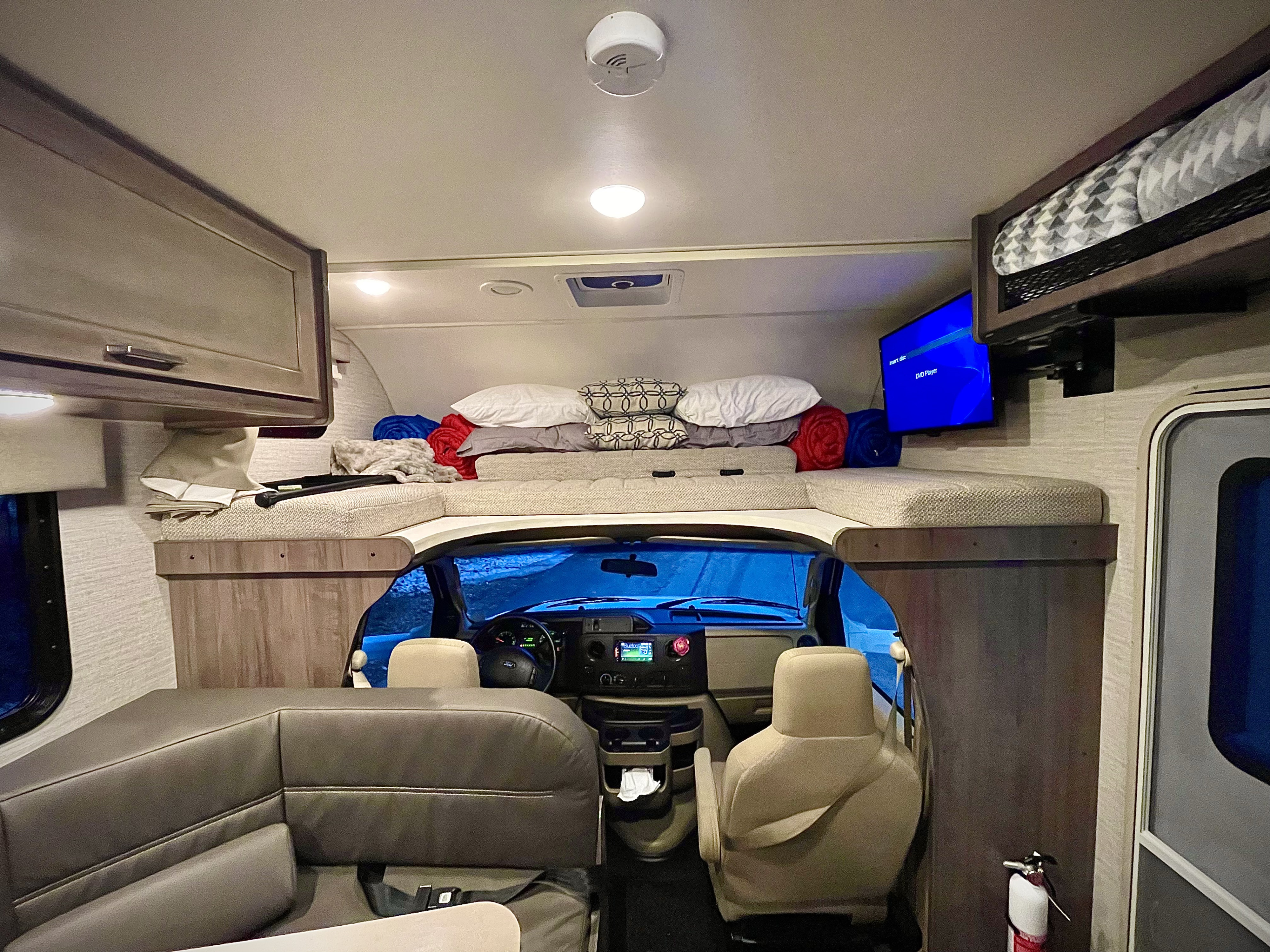 Inside an RV rental: a spacious overhead bunk, driver's cabin, dinette, and TV for your road trip.. Winnebago Minnie Winnie 2020