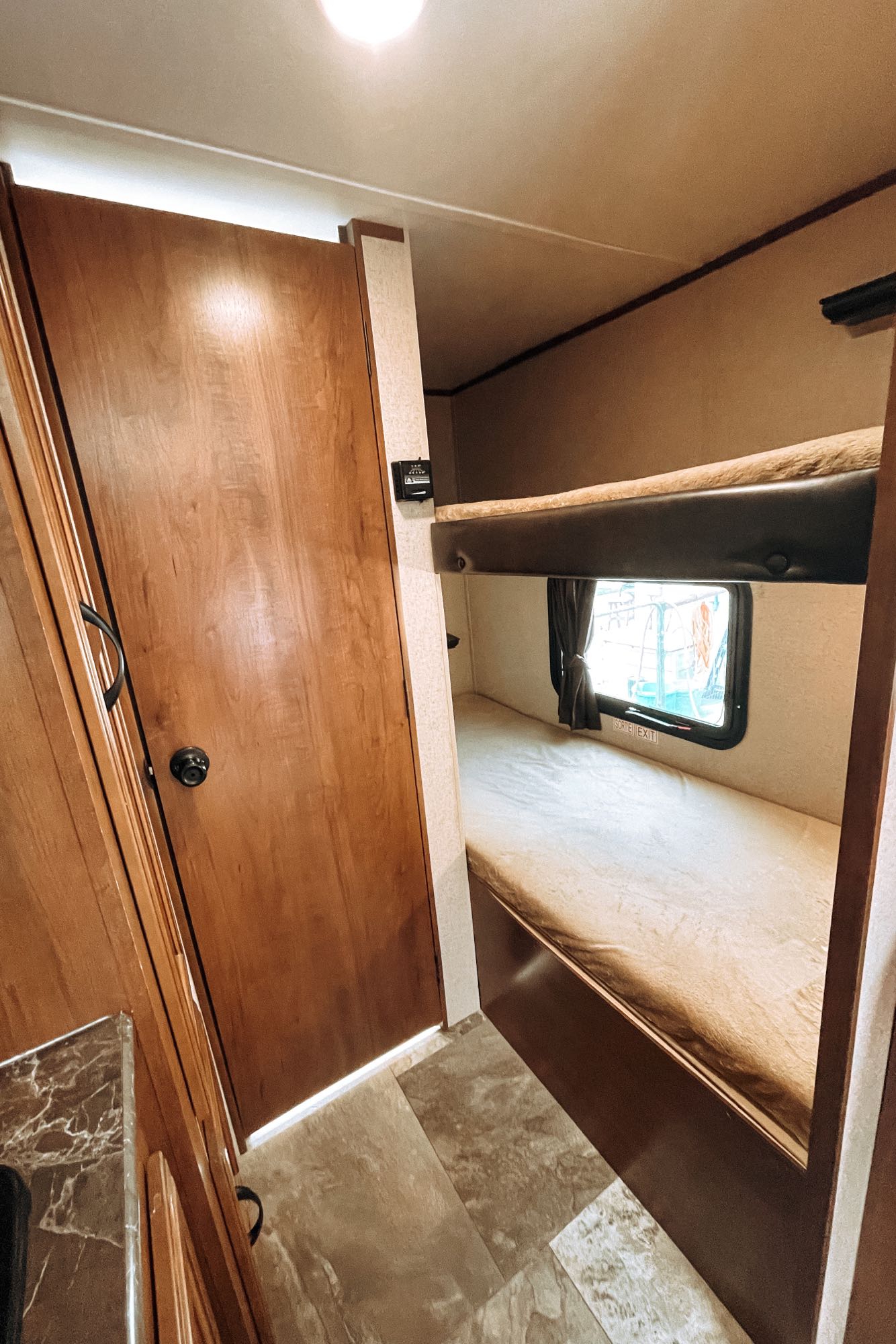 Cozy RV rental interior. Bunk beds with an emergency exit window are on the right, a wooden door is on the left.. Jayco Jay Flight SLX 2016