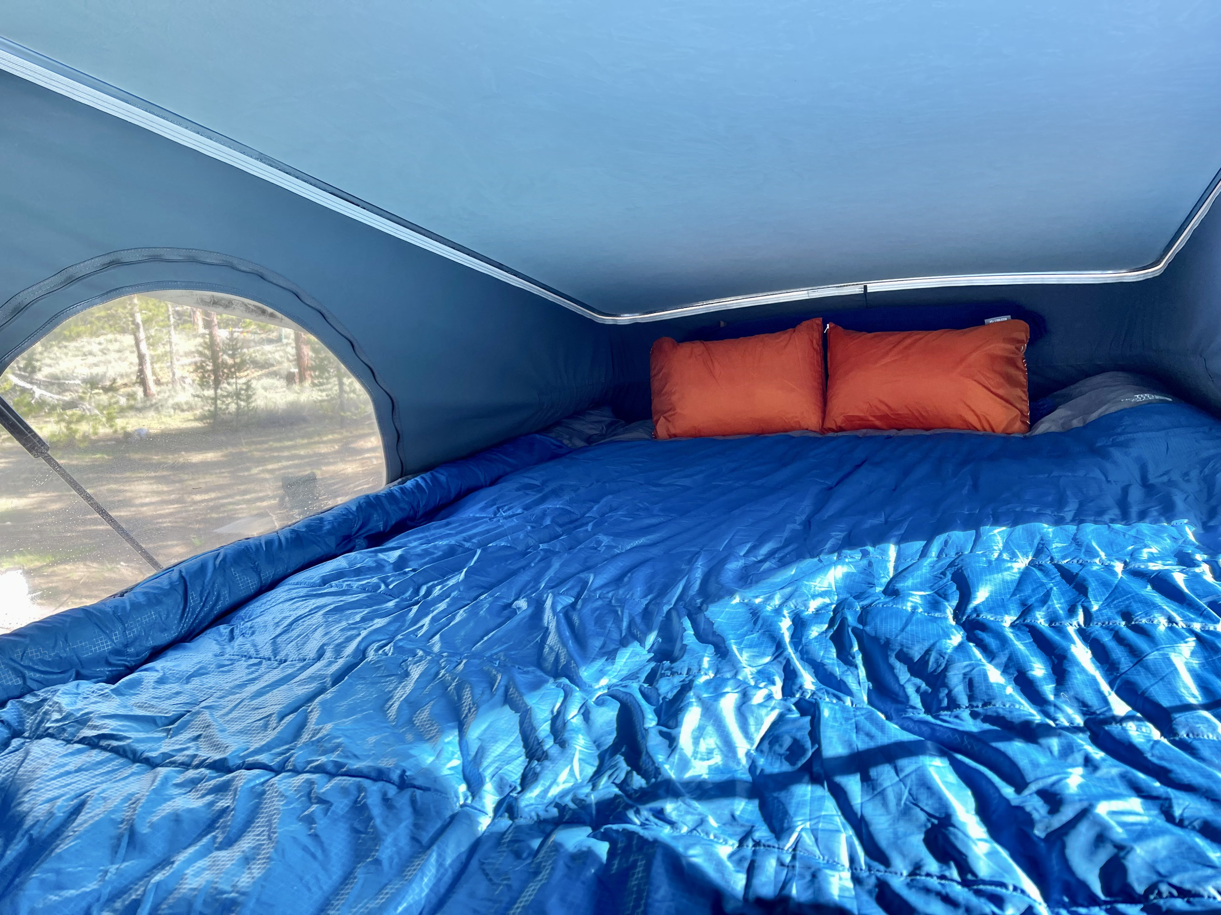 Cozy pop-top **rv rental** camper bed with blue sleeping bag and orange pillows, offering an outdoor view. Ideal for **camping**.. Winnebago Solis 2022