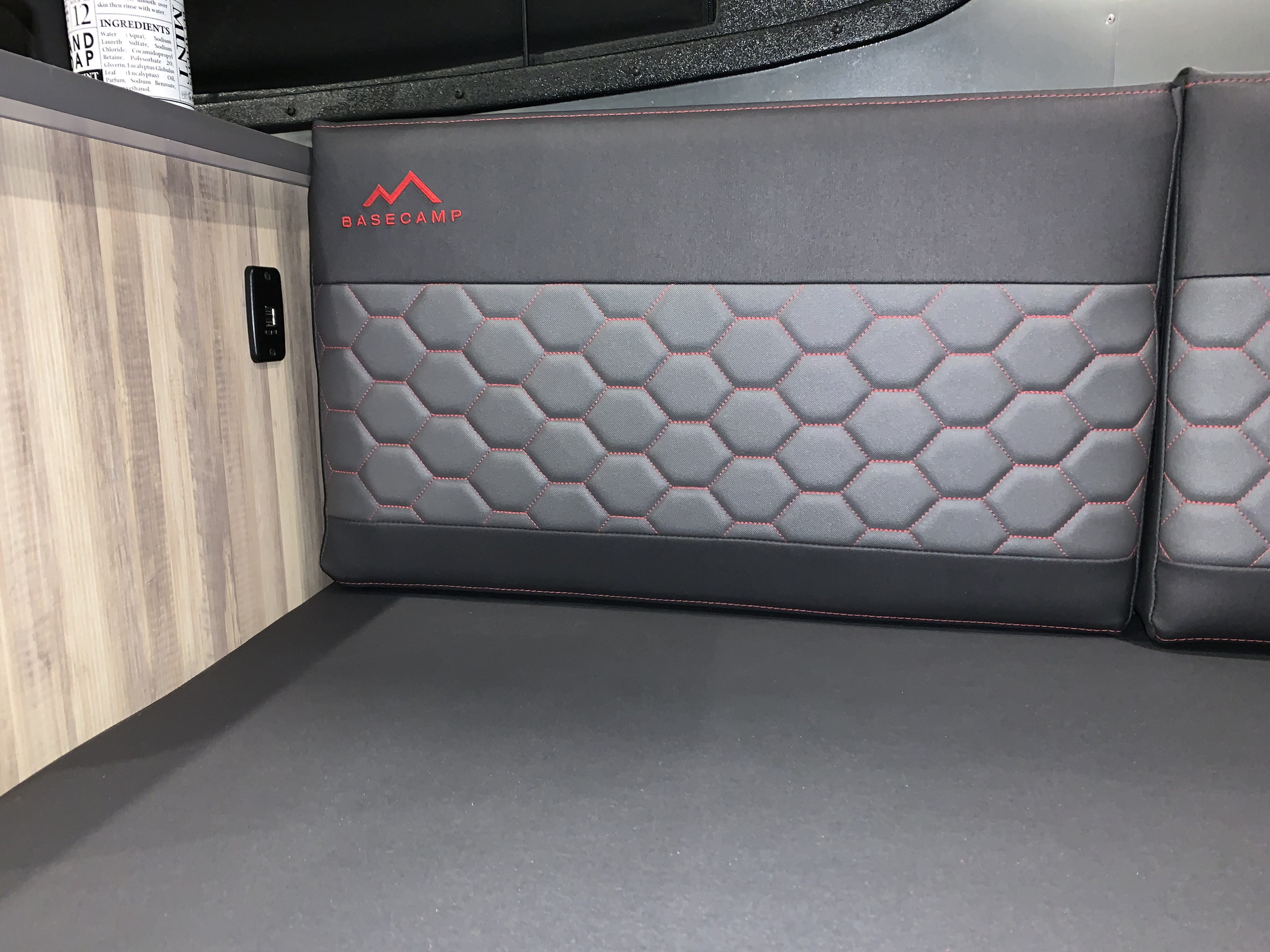 Inside an rv rental: stylish BASECAMP seating with hexagonal red stitching, wood paneling, and a convenient USB port.. Airstream Basecamp 2021