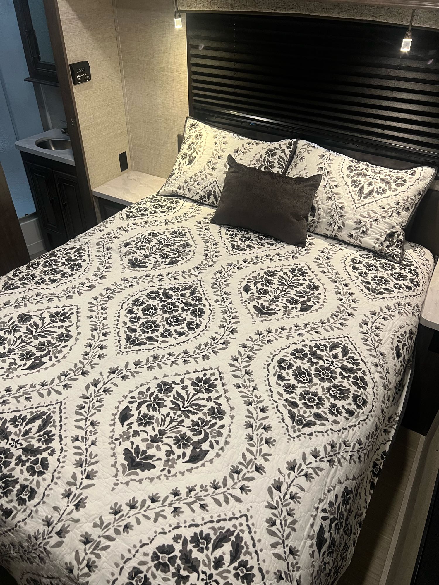RV rental interior: A cozy bedroom with a patterned bed quilt, dark headboard, and a vanity sink visible on the left.. Entegra Coach Odyssey 2022