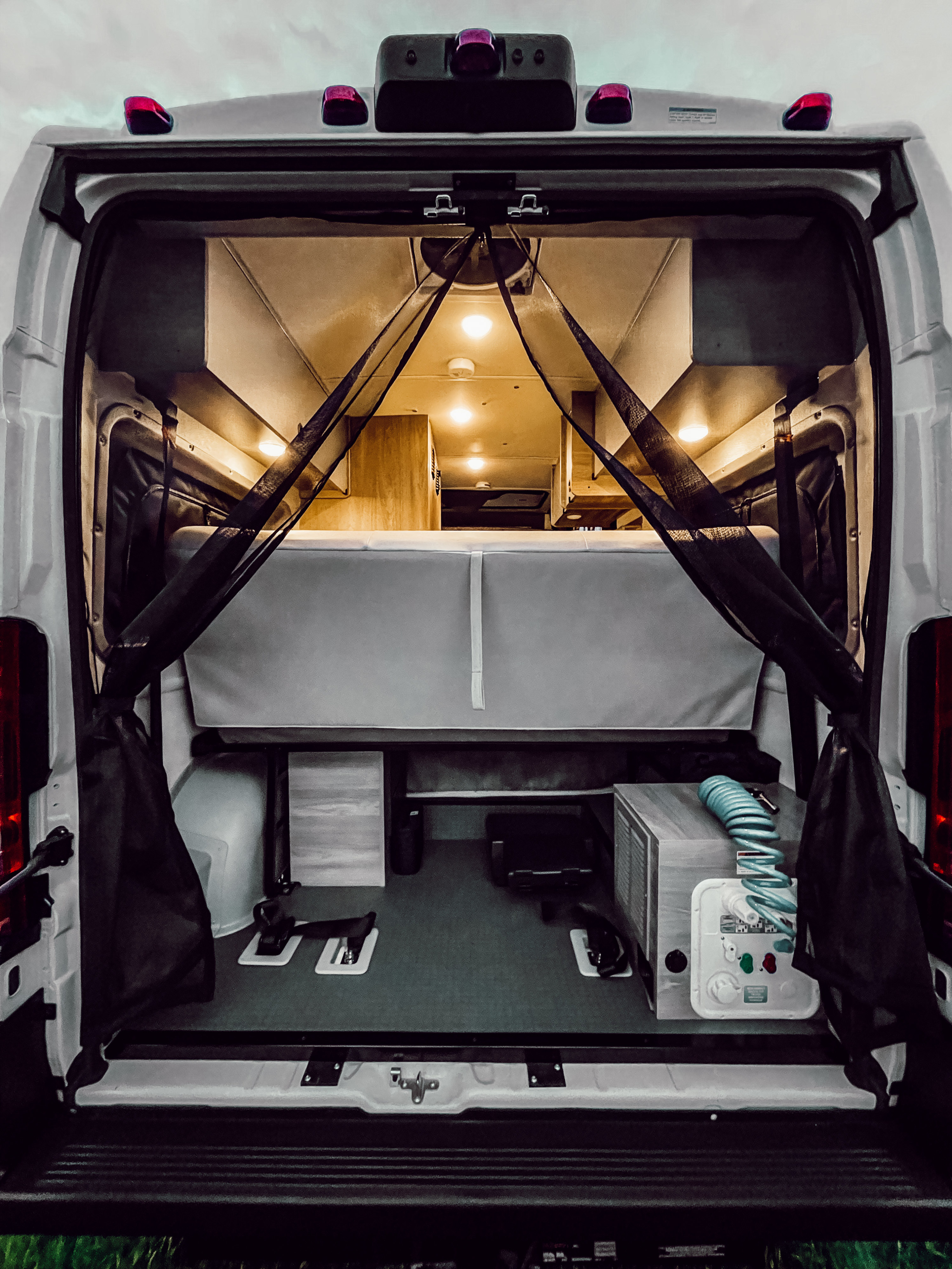 Inside an RV rental, this camper van's cozy bed, storage, and utility setup are visible from the open back.. Winnebago Solis 2022