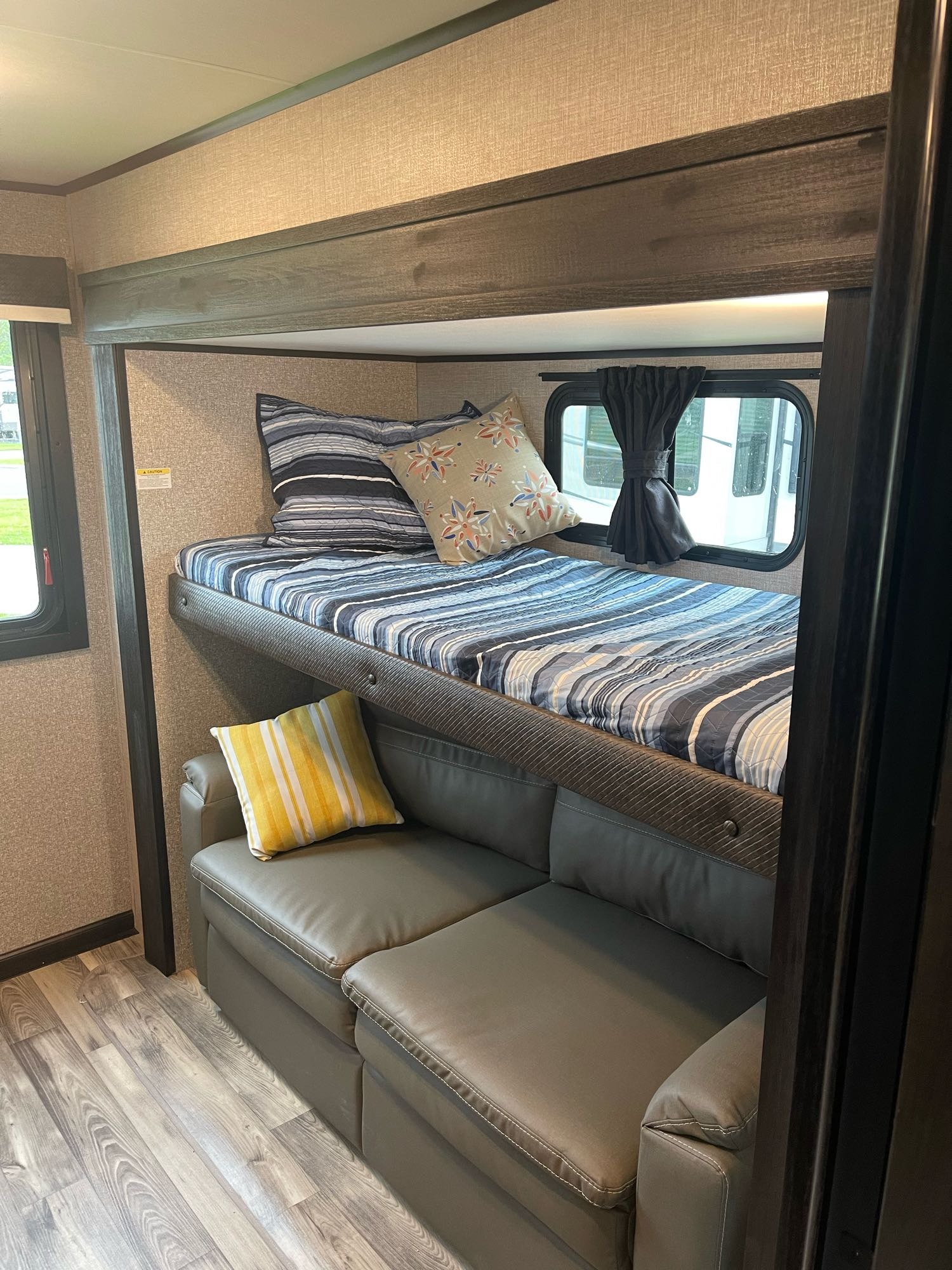 RV rental bunk bed and sofa area. Cozy, compact interior featuring an upper bunk with striped bedding and a lower grey sofa.. Jayco Eagle HT 312BHOK 2022