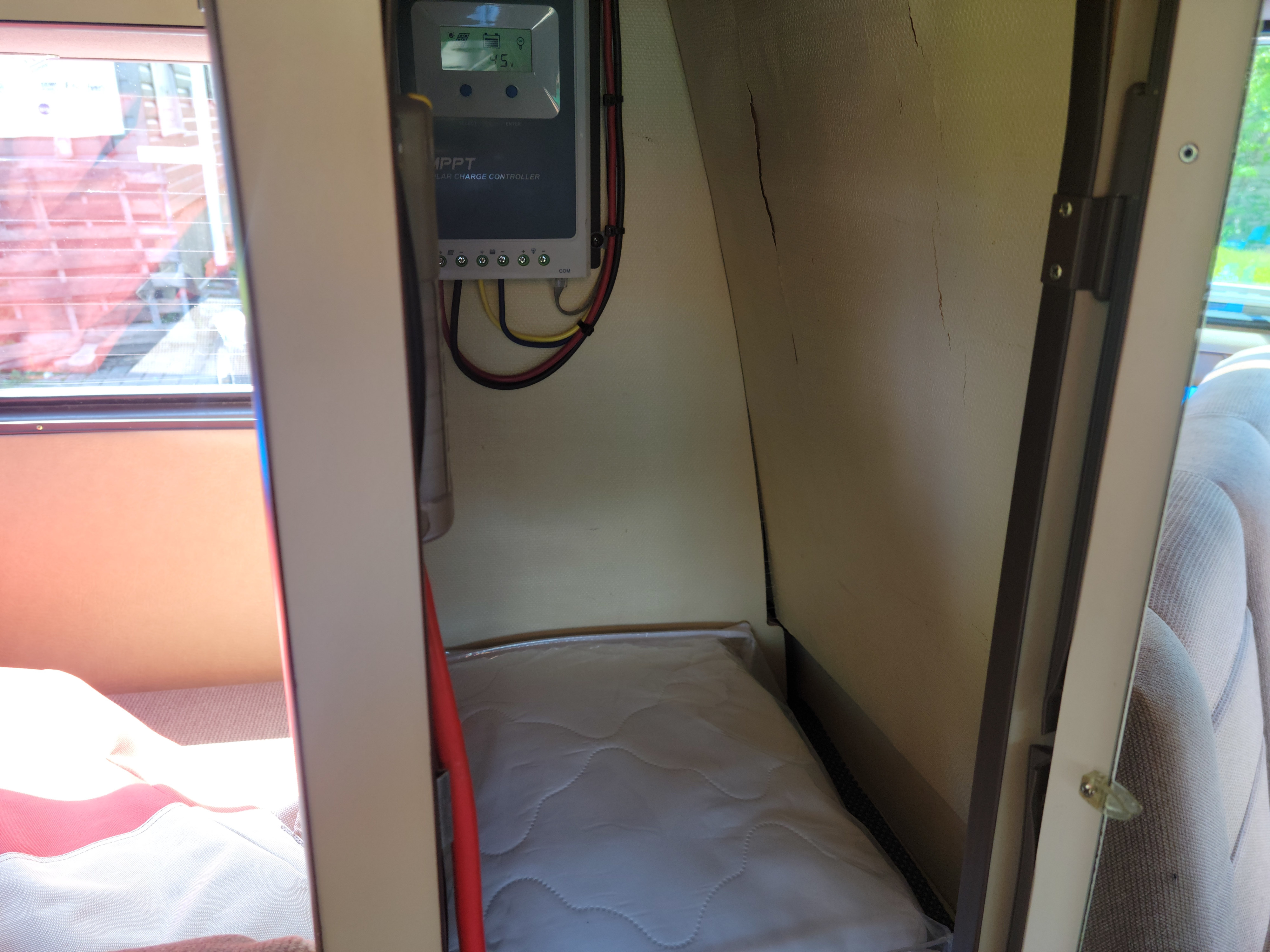This RV rental's interior features an MPPT solar charge controller, a mattress, and a window view, despite wall cracks.. Volkswagen Westfalia 1986