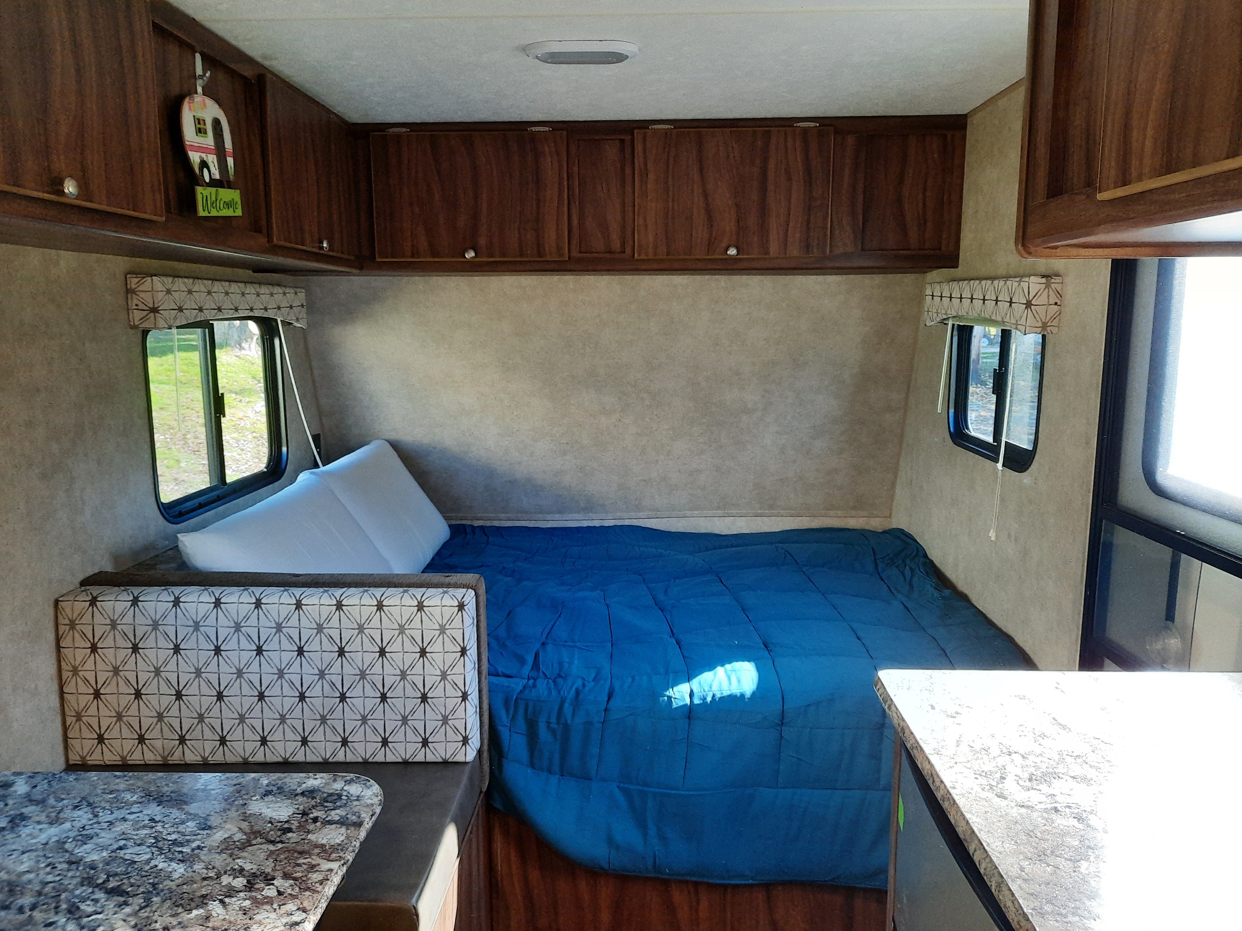 Inside a cozy RV rental, featuring a bed with blue bedding, patterned seating, and wood cabinets. Ready for your next camping trip!. Forest River Viking Saga 2016