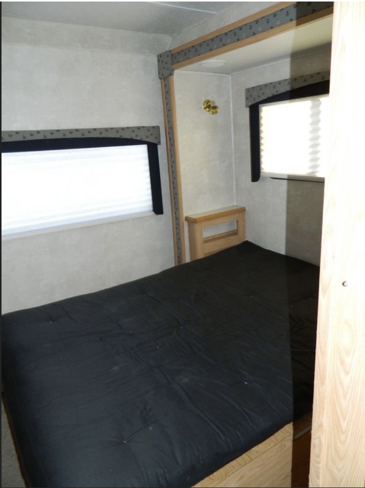 RV rental bedroom: a cozy sleeping area featuring a black mattress & two windows with blinds in a light-toned interior.. Forest River Sunseeker LE 2005