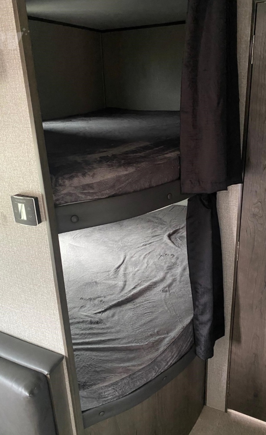 Cozy dark grey bunk beds in an RV rental, offering comfortable sleeping with privacy curtains & a Dometic thermostat.. Jayco Jay Flight SLX 2020
