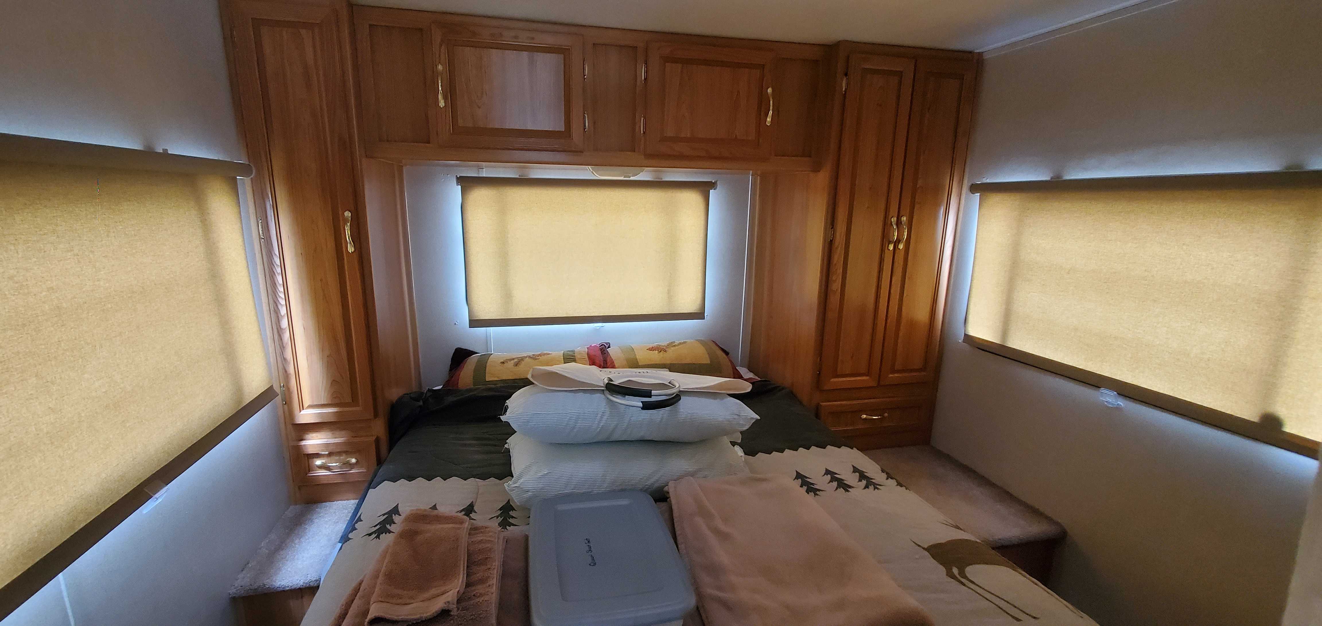 Cozy RV rental bedroom with warm wooden cabinets, a comfy bed, and blinds on three windows for your travels.. Coachmen Leprechaun 2000