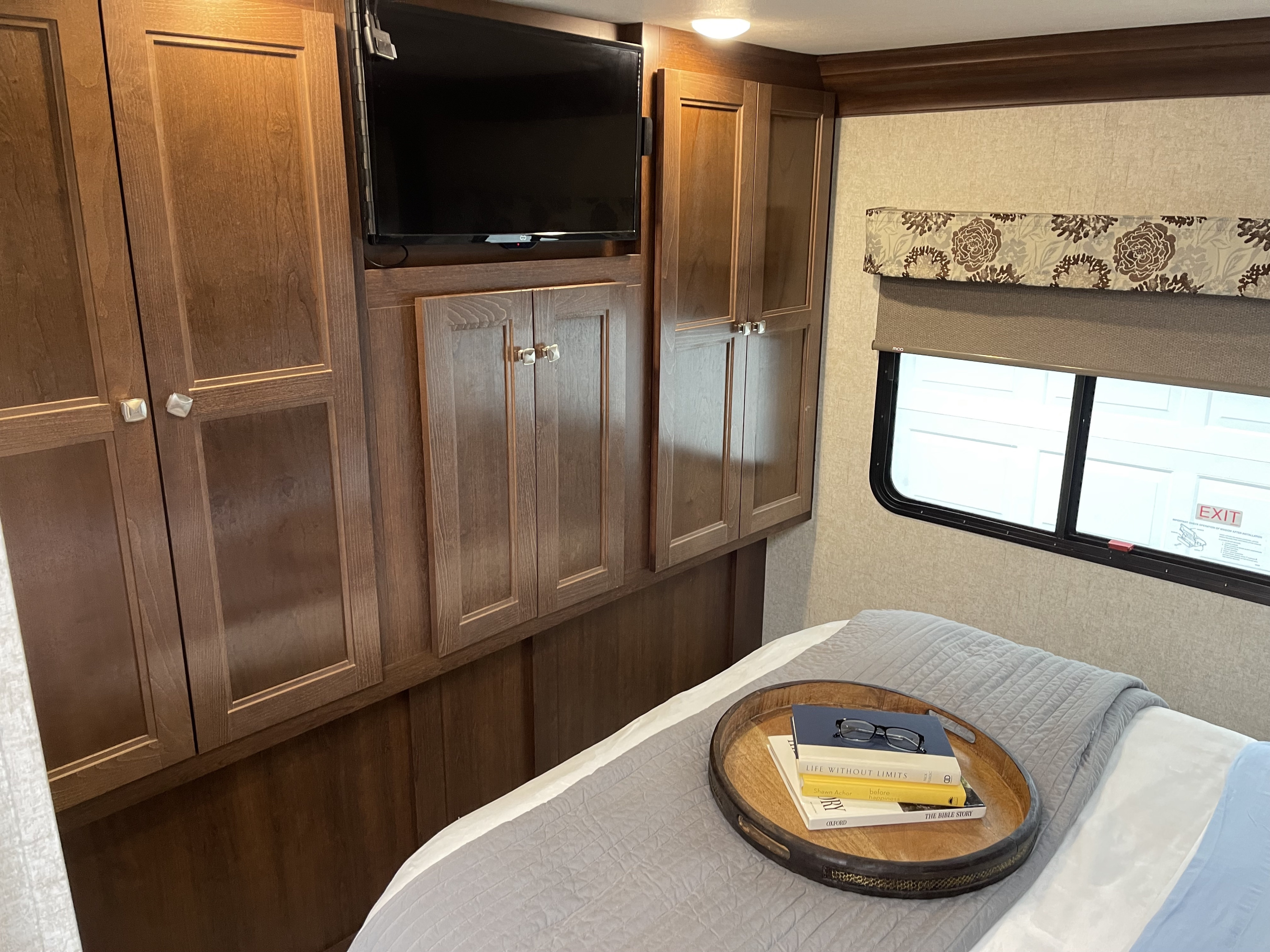 Cozy RV rental bedroom with wooden cabinets, wall-mounted TV, bed with books, and a window for comfortable stays.. Forest River Forester 3051 2019