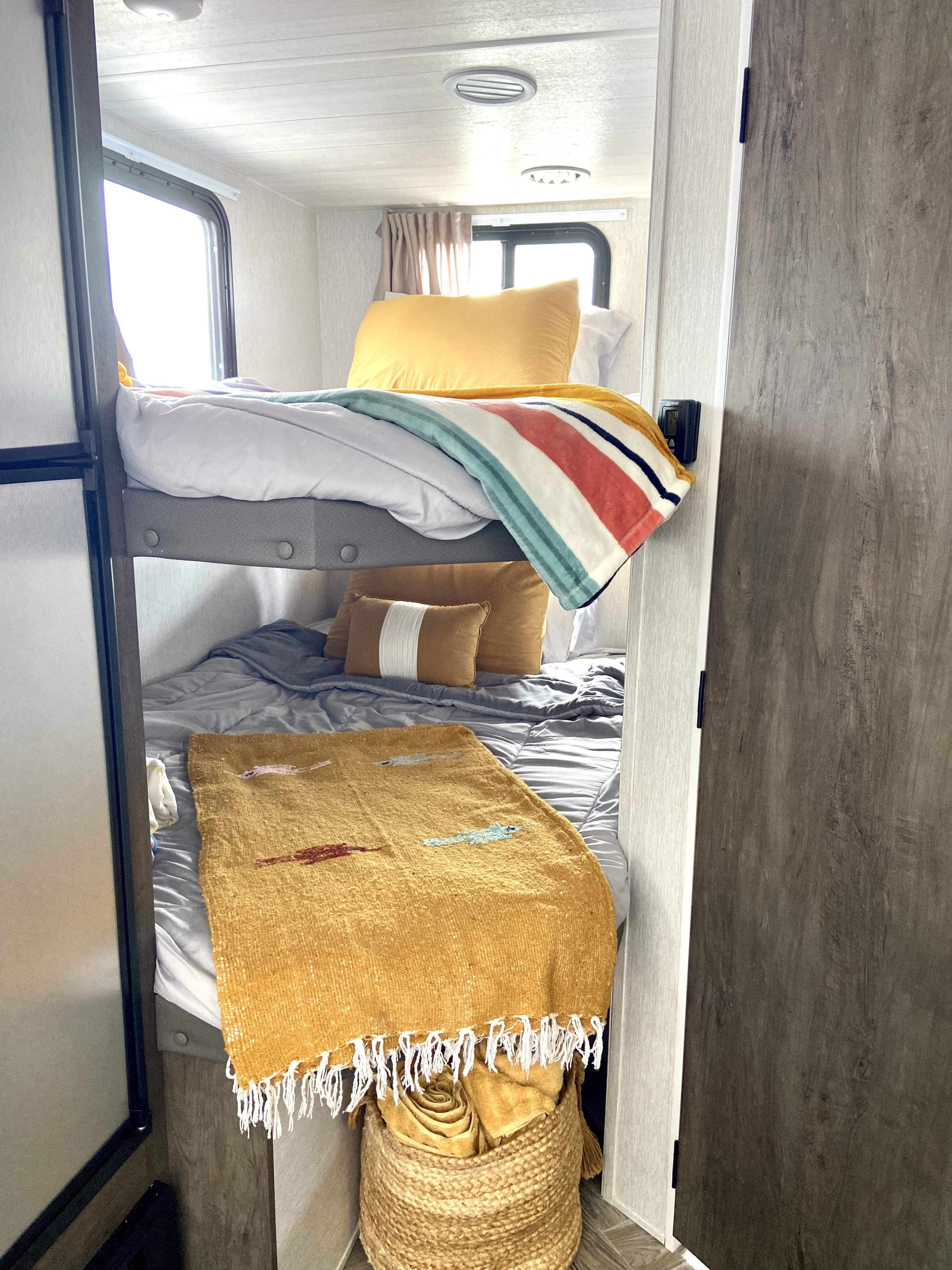 Bright RV rental bunk beds feature cozy yellow pillows, a striped blanket, and a woven basket for homey comfort.. Forest River Salem Hemisphere 2022