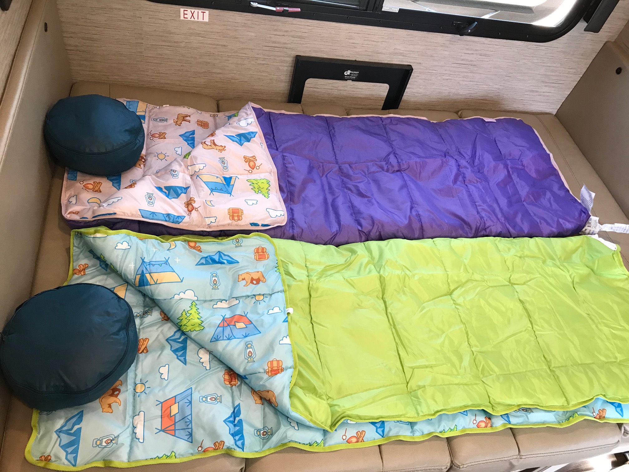 Two kids' patterned sleeping bags and pillows are laid out in an RV rental, set for cozy travel adventures.. Thor Compass 2022
