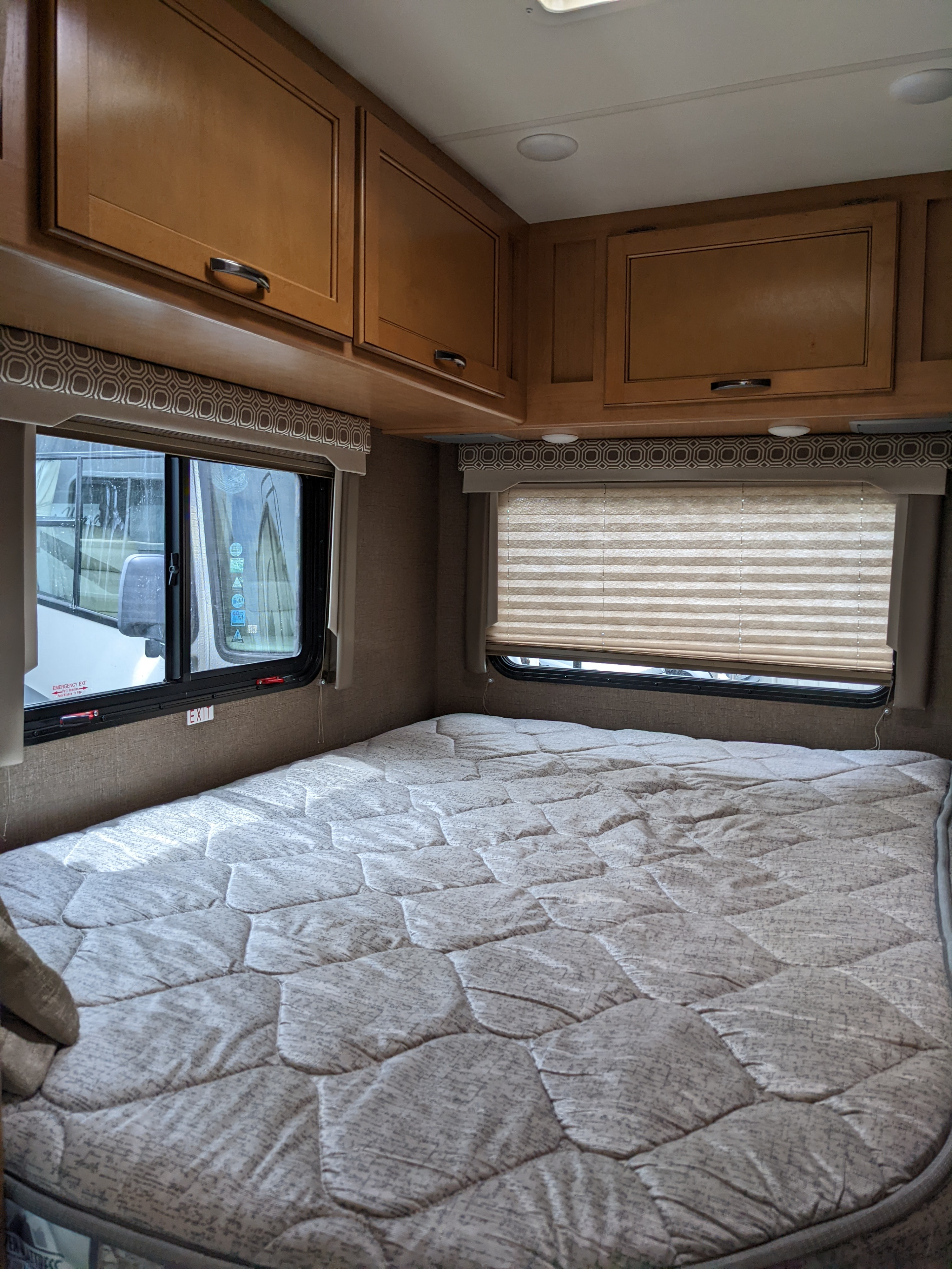 RV rental bedroom interior featuring a comfortable bed, overhead cabinets, and windows with patterned valances and shades.. Thor Motor Coach Four Winds 2017