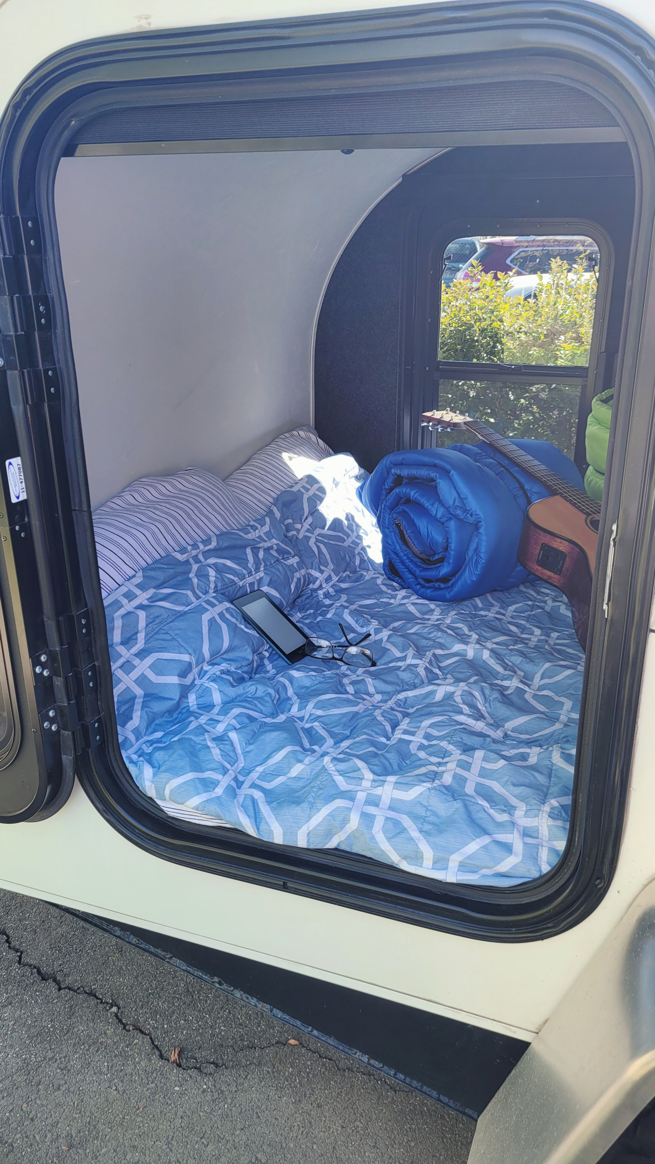 Cozy RV rental interior with a bed, blue bedding, phone, glasses, guitar, & rolled sleeping bag. Ready for adventure!. Little Guy Other 2012