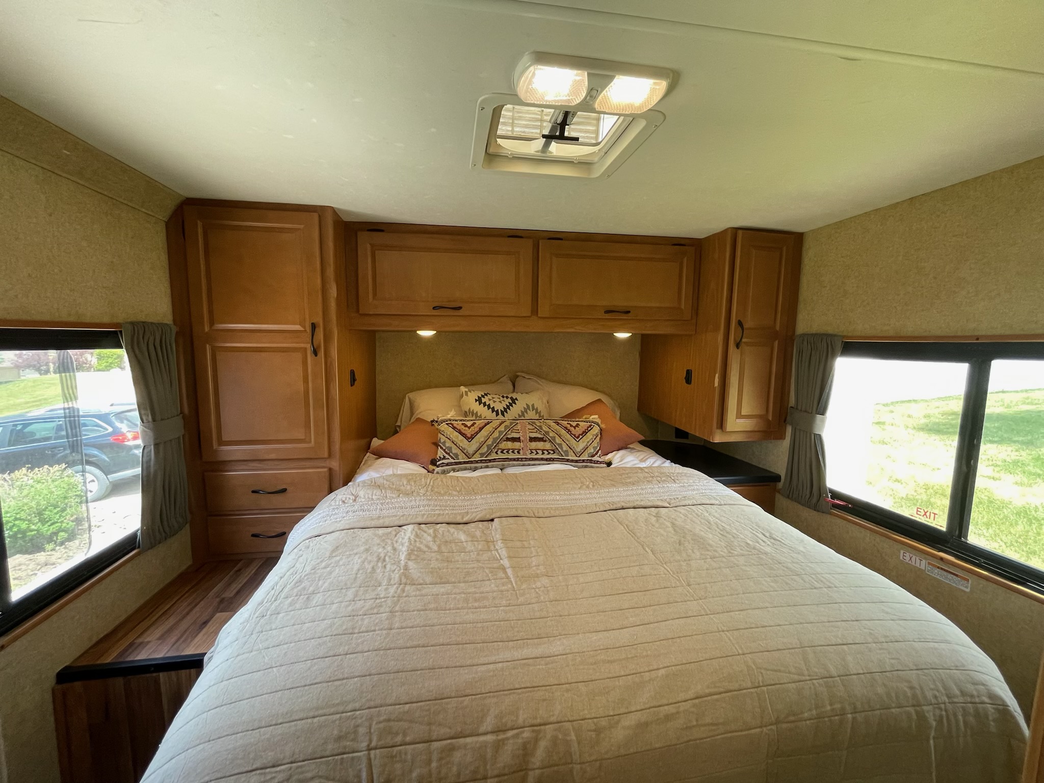 Spacious RV rental bedroom with cozy bed, wood cabinetry, and natural light from side windows. Perfect for travel.. Thor Majestic 2017