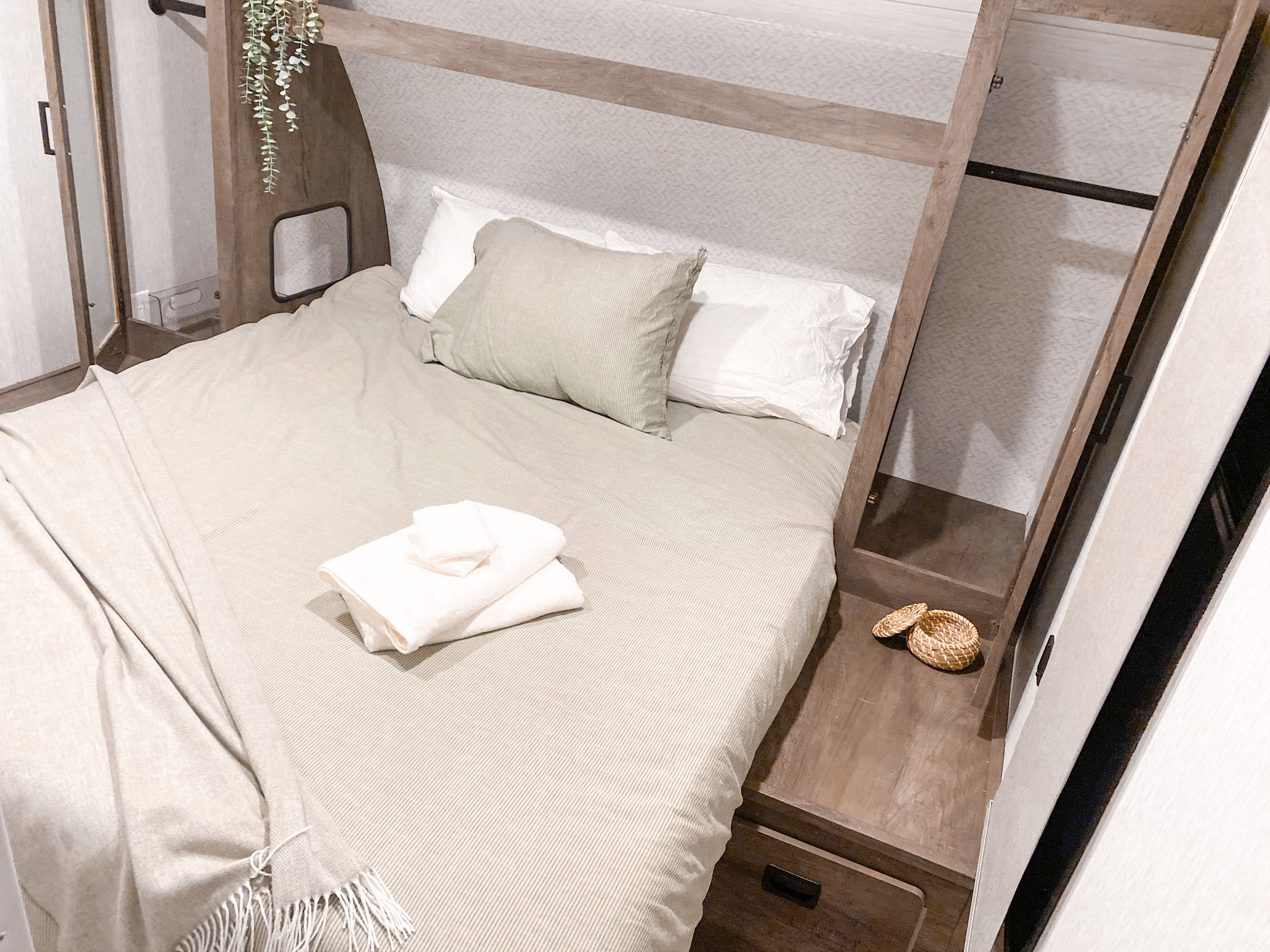 A bright, cozy RV rental bedroom with light striped bedding, integrated storage, and thoughtful decor like plants.. Forest River Salem Cruise Lite 2022